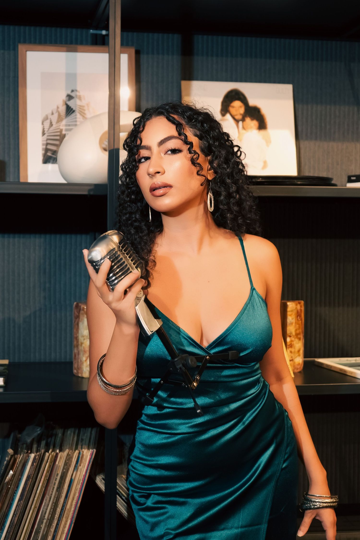 A singer in a teal satin dress performs at a lounge venue with vinyl records displayed in the background.