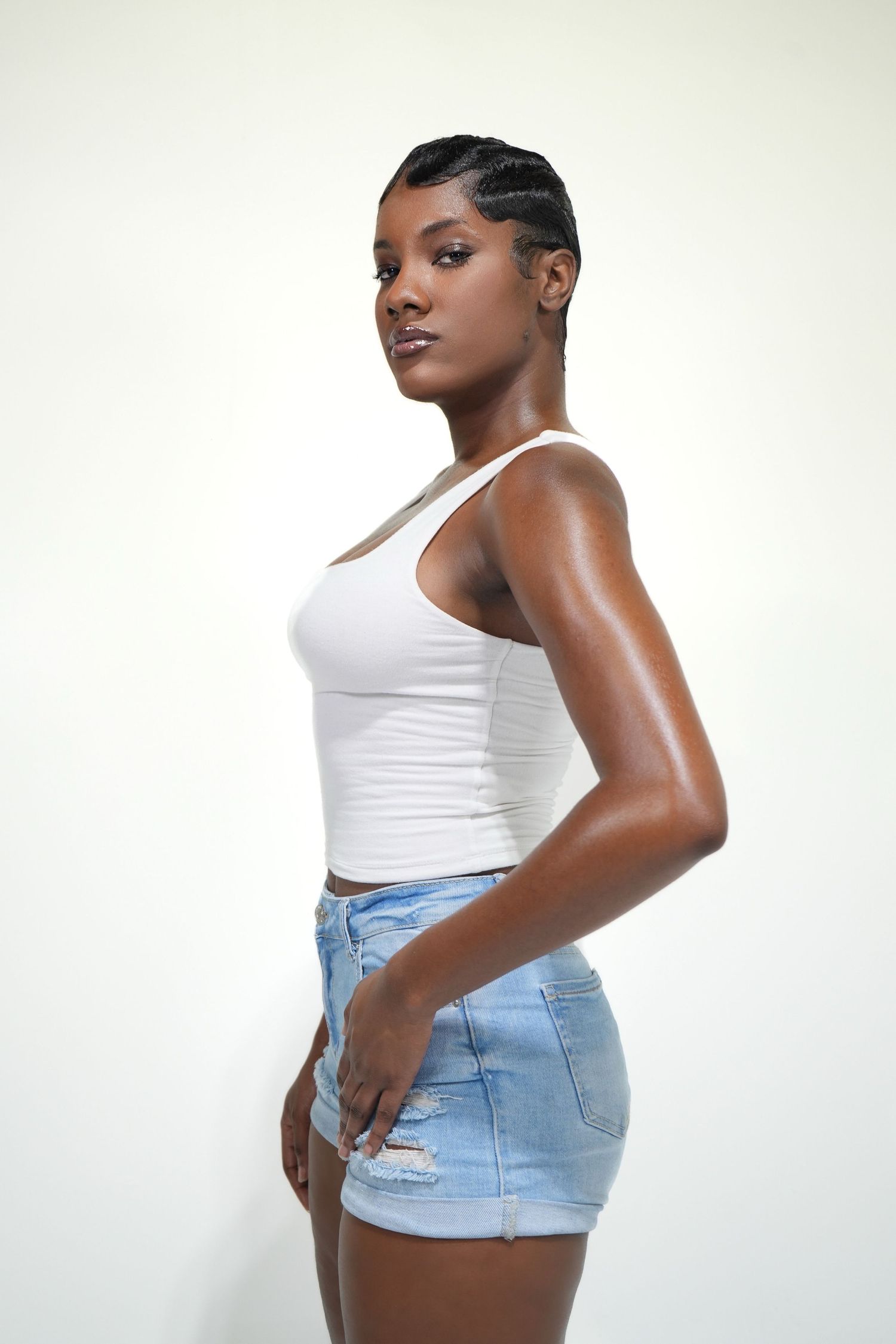 Side view poses showing white tank top and light wash denim shorts against neutral backdrop.