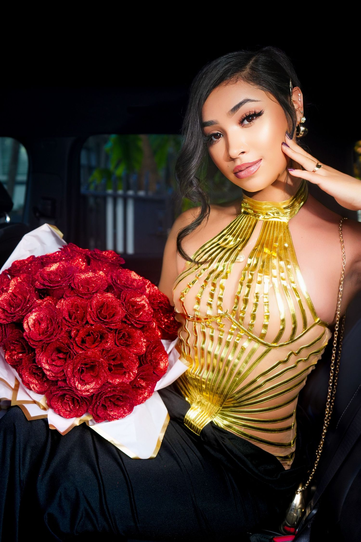 A person in a metallic gold top holds a vibrant bouquet of red roses in a car.