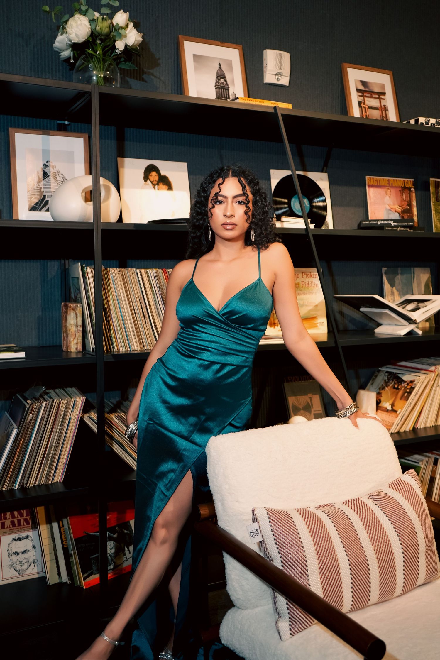 A series of photos showing someone in a teal silk dress reclining on a couch near bookshelves in a moody interior setting.