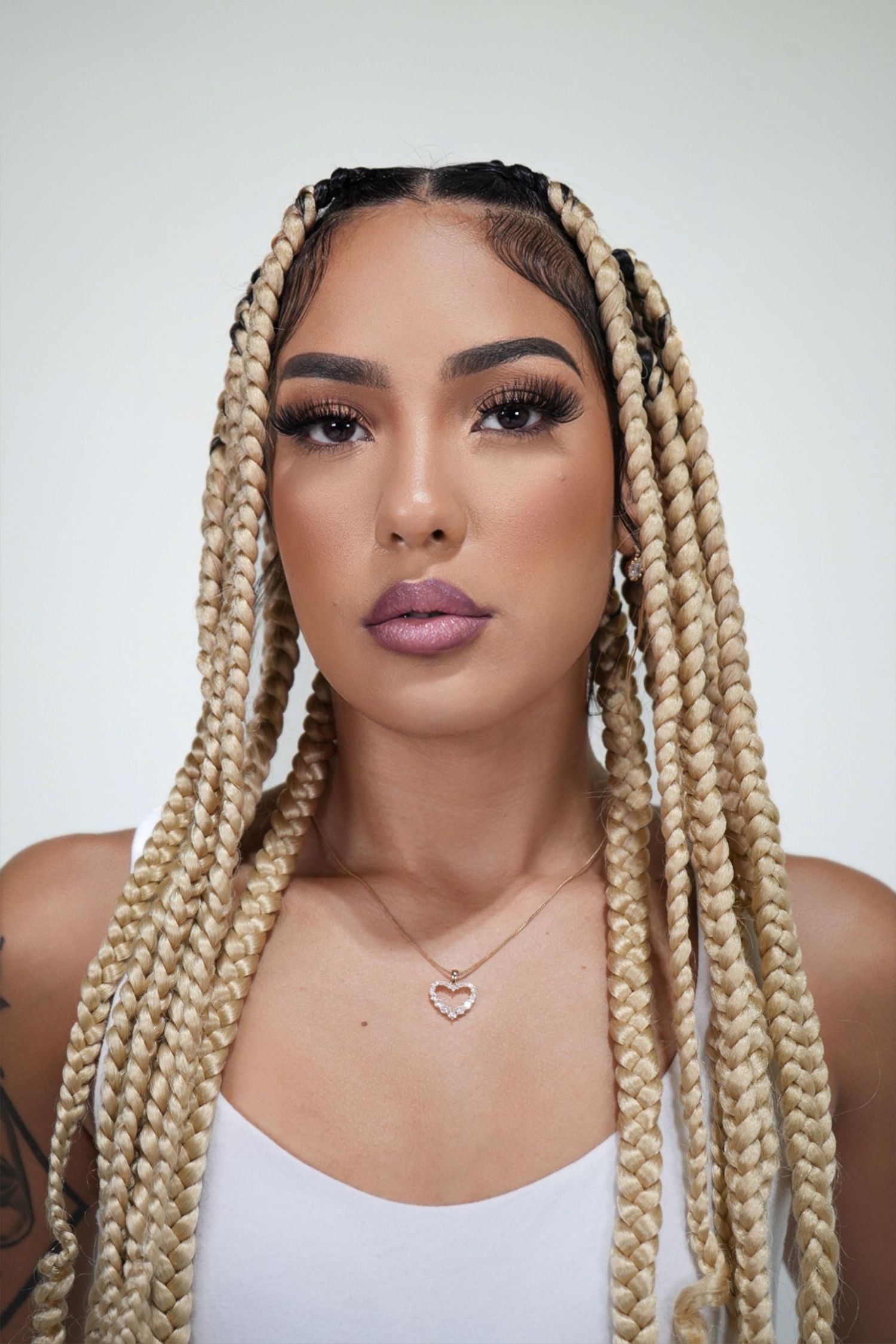 A series of beauty shots showing blonde box braids, glossy mauve lipstick, and white tank top styling.