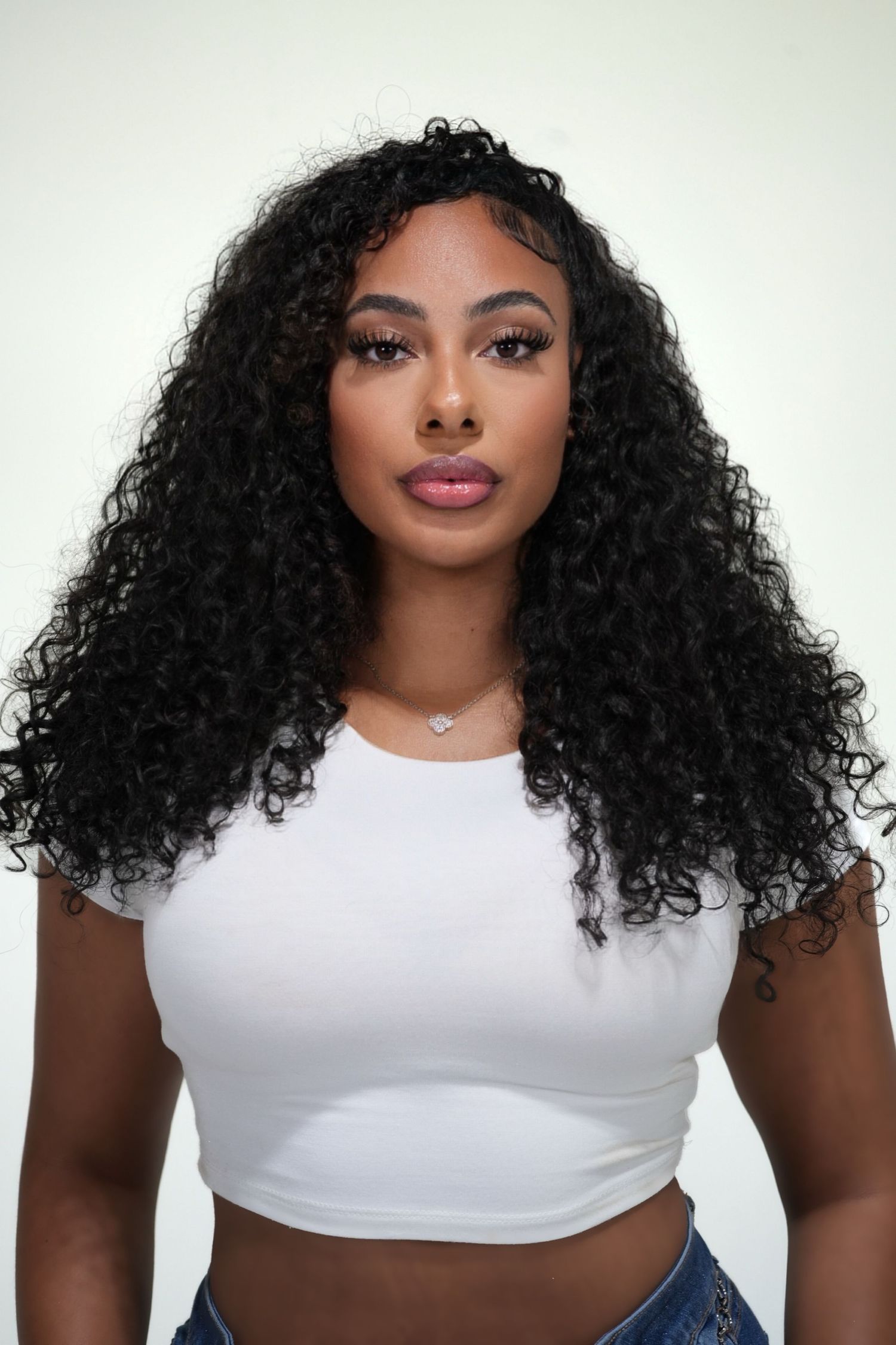 Four photos showing a model with voluminous curly hair wearing a white crop top against a light background.