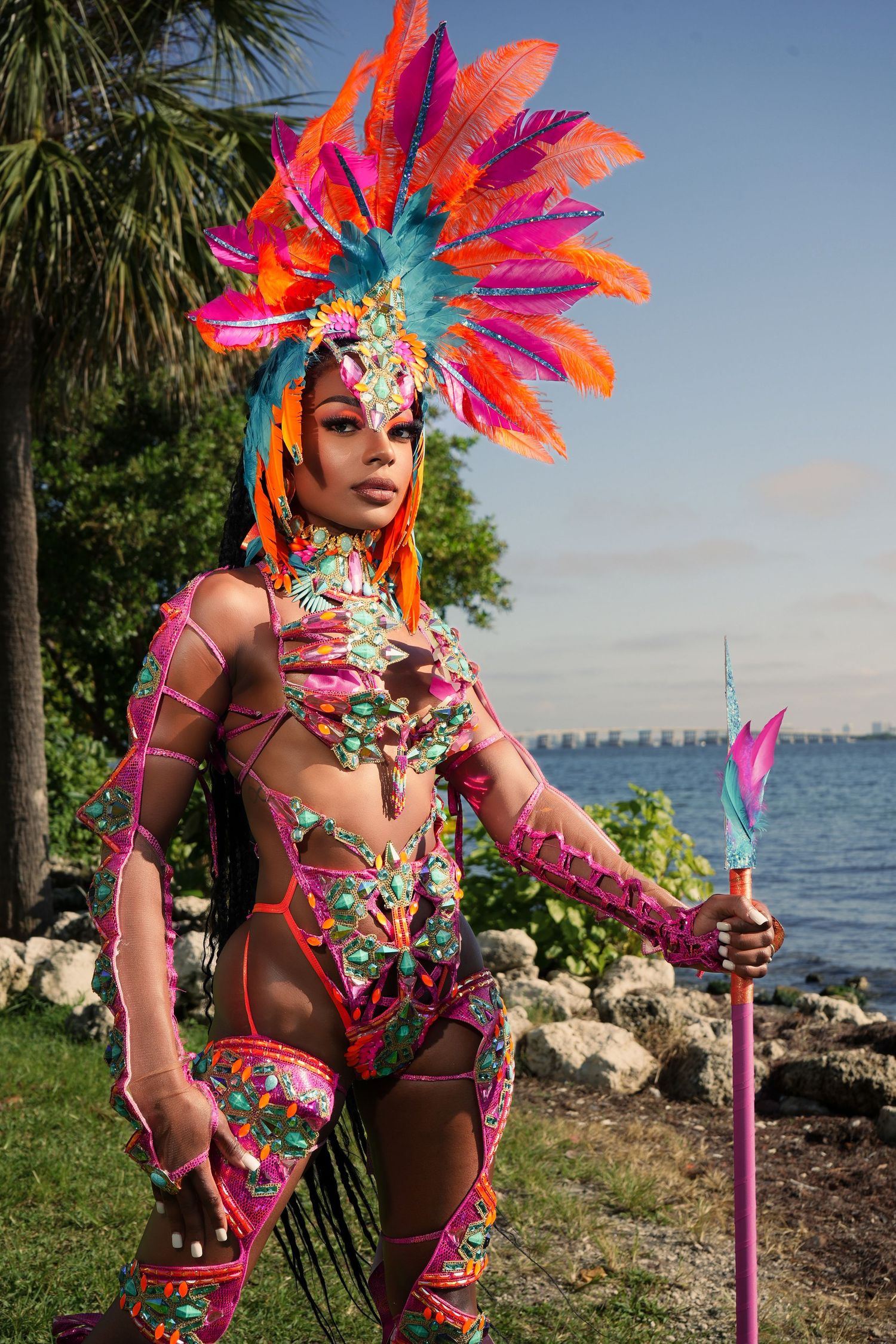 Colorful feathered carnival costume with bright pink accessories photographed against a coastal landscape.
