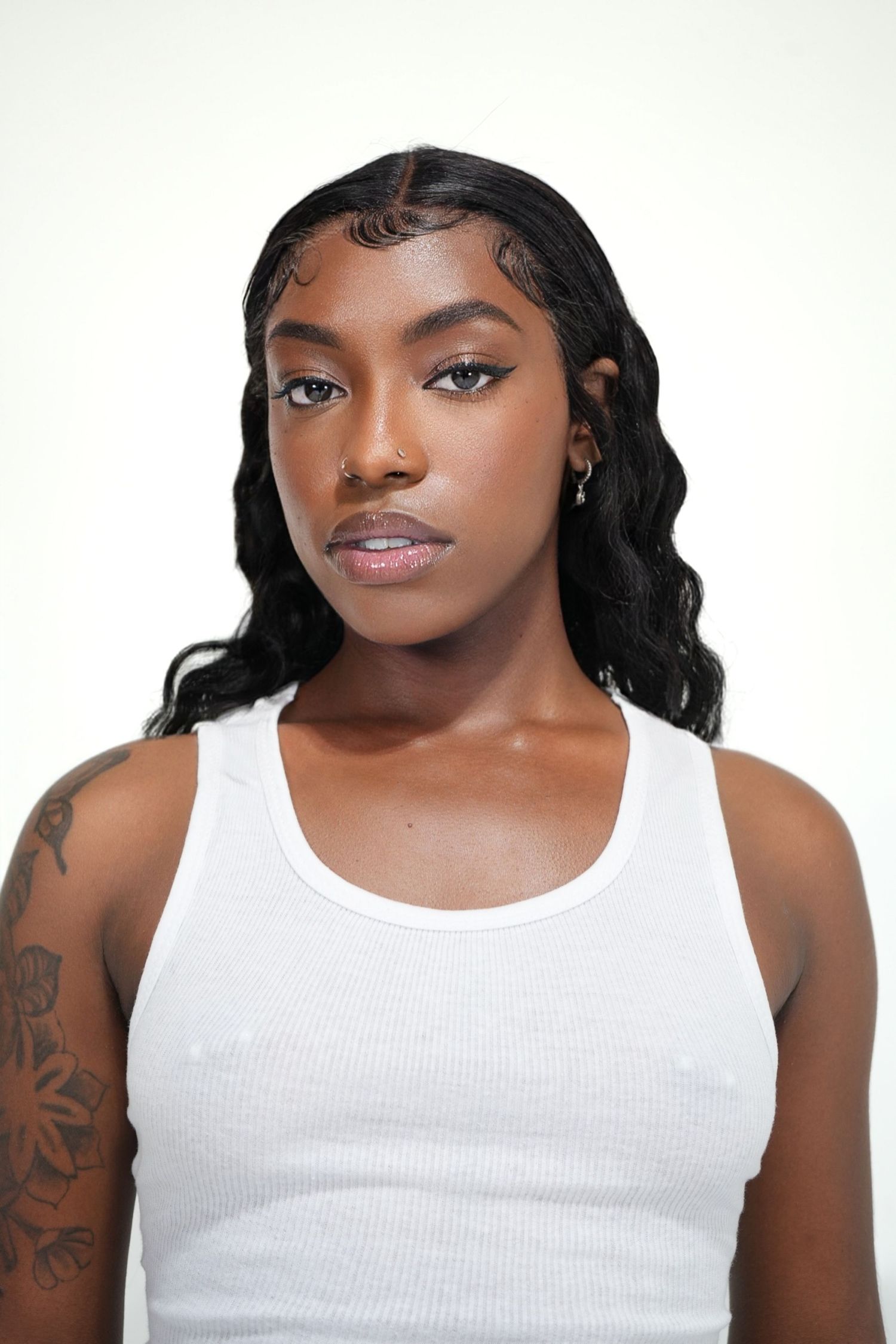 Close up portrait of model in white ribbed tank top with wavy hair and natural makeup.