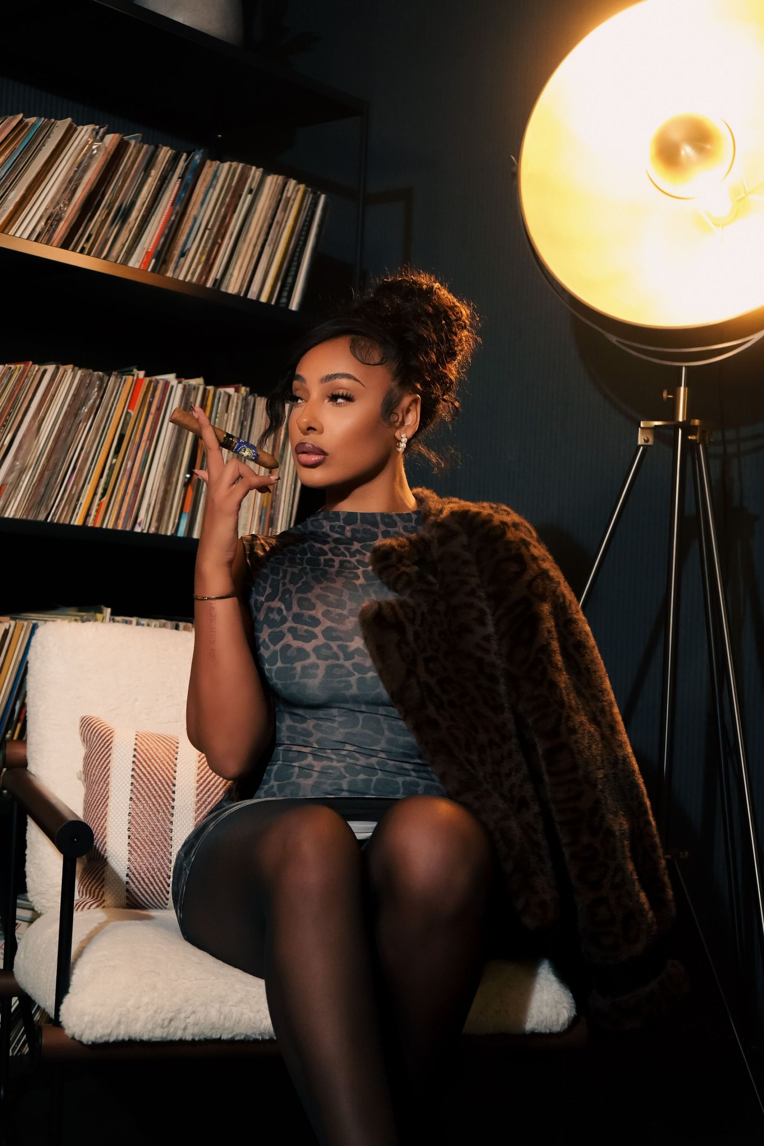 A moody boudoir photoshoot features dramatic lighting from a floor lamp against a backdrop of vinyl records.