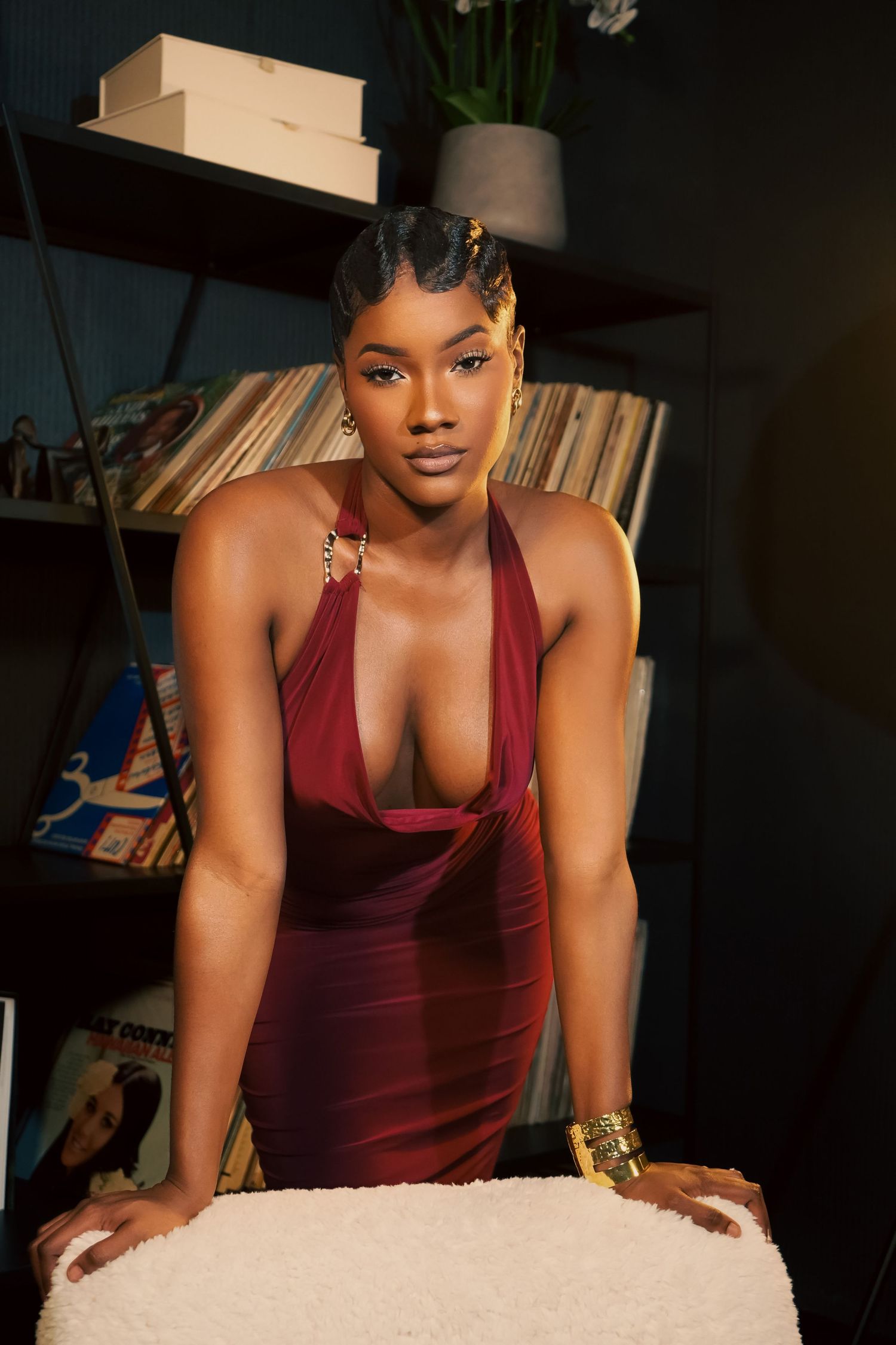 A woman in a burgundy velvet dress poses against a dark background with dramatic lighting.