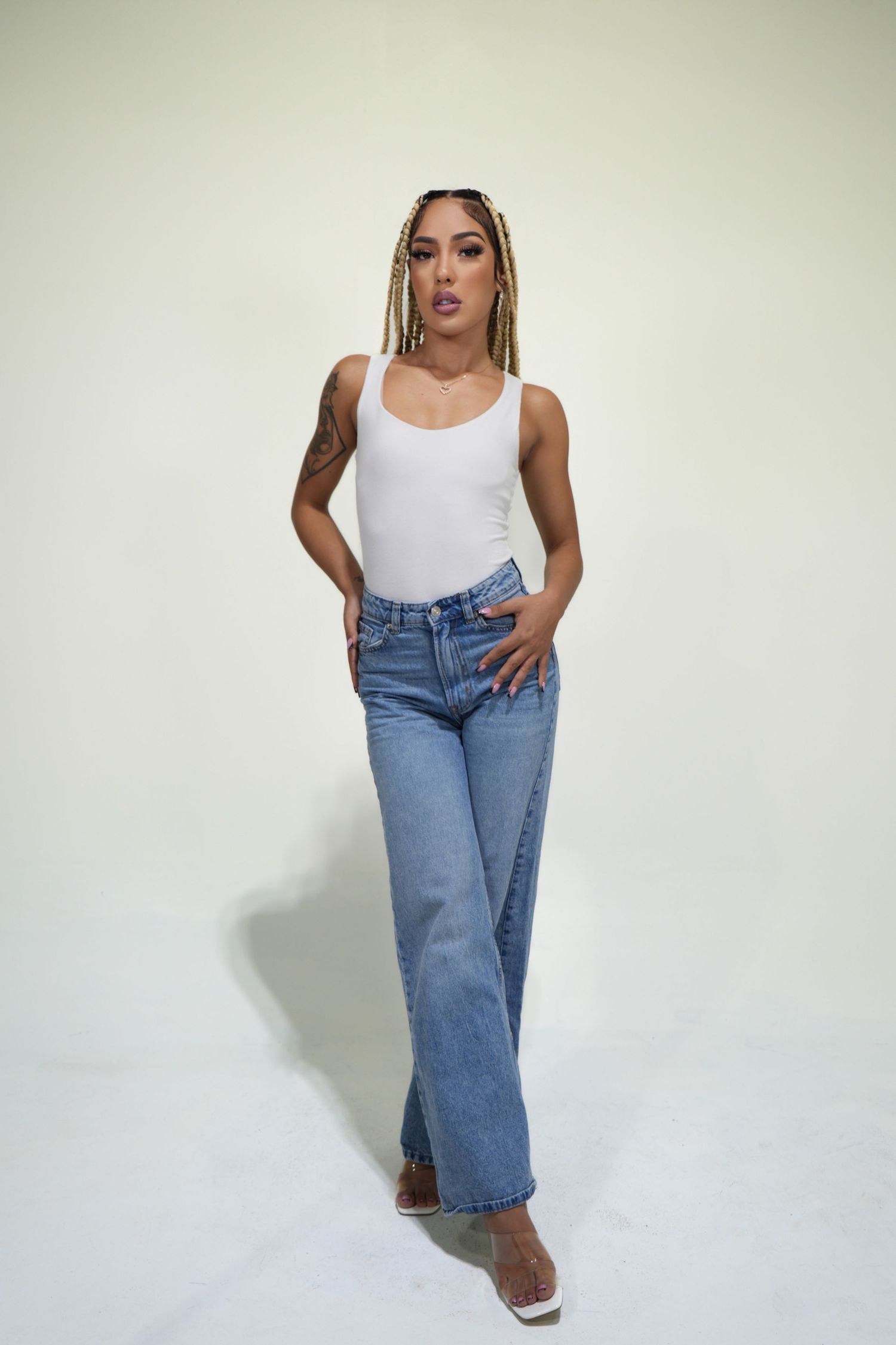 A model poses in a casual white tank top and light blue flared jeans against a plain white background.