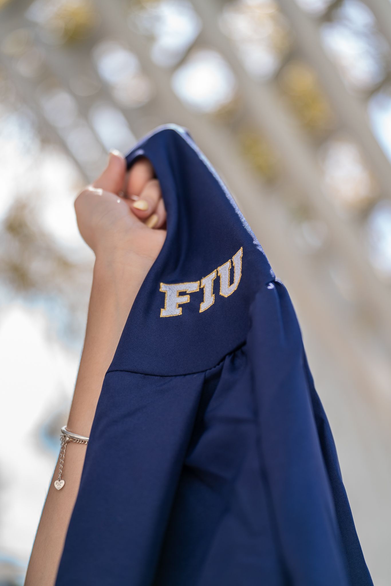 Close-up view of a navy blue FIU graduation gown with embroidered university letters against a blurred background.