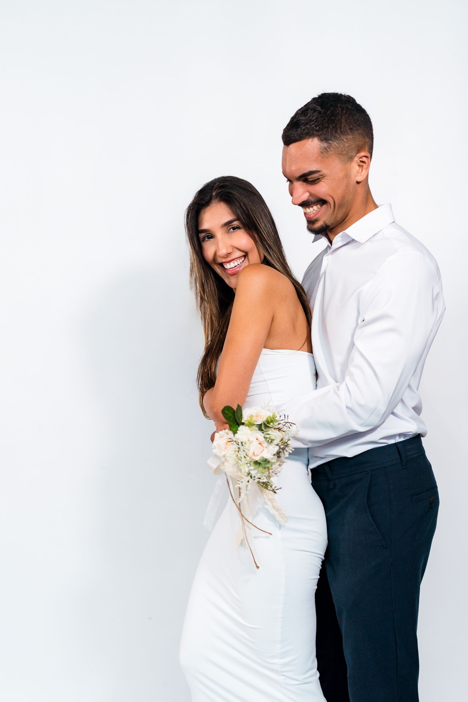 A couple in white and navy formal attire share a romantic moment against a white background.