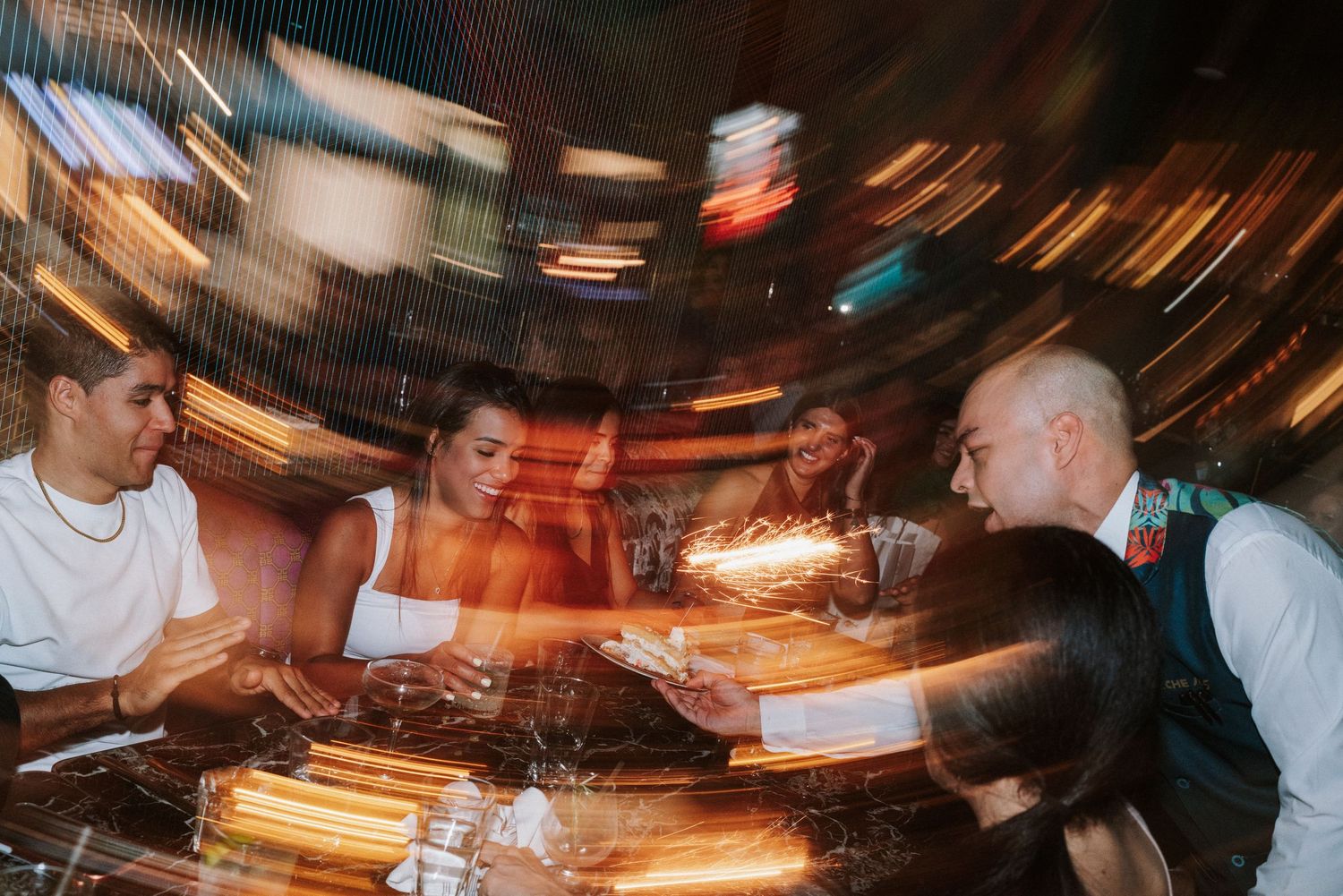 Motion blur photo of people sitting at a bar counter with dramatic lighting and streaks of movement captured in frame.