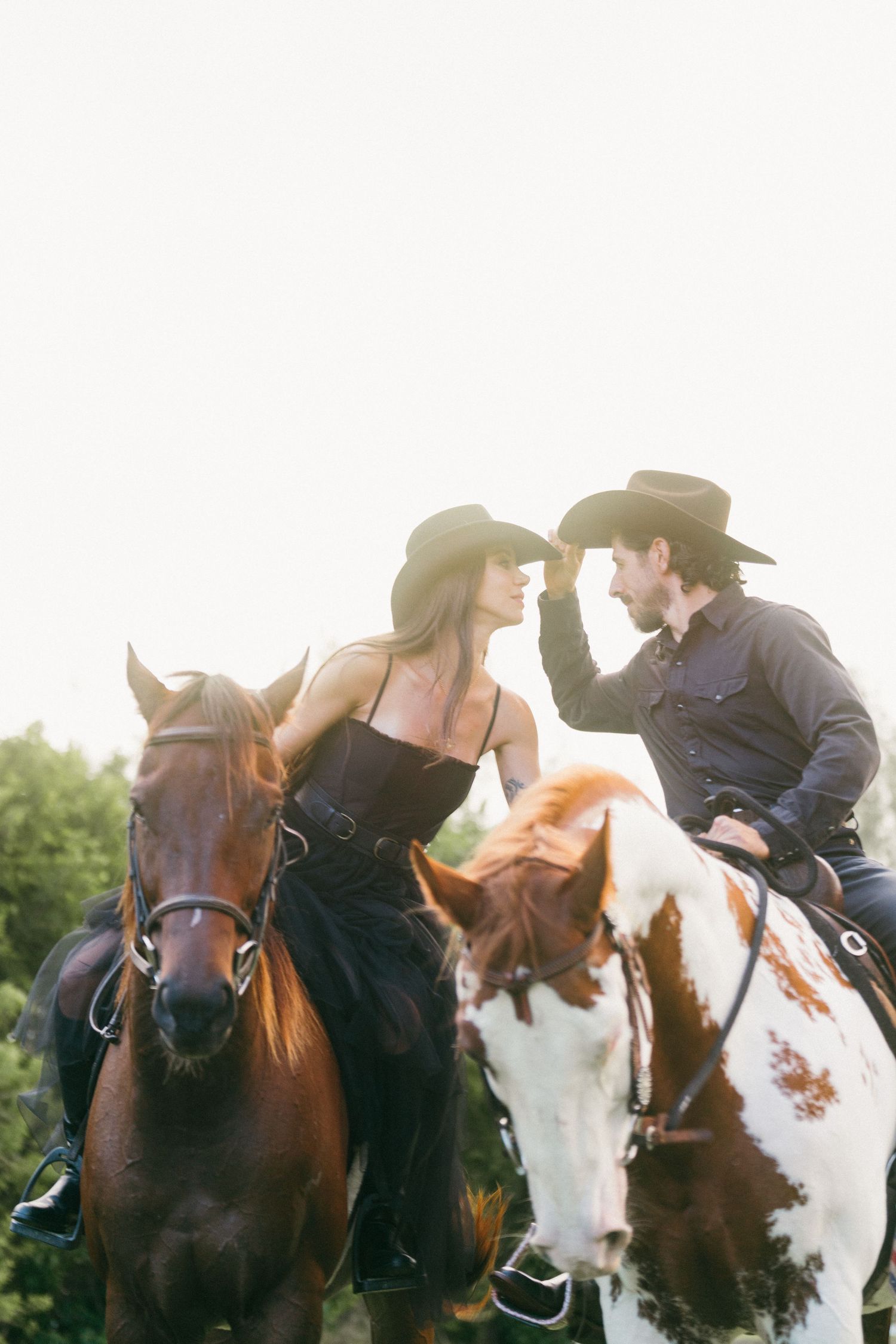 A romantic couple in western attire share tender moments while horseback riding through scenic countryside.