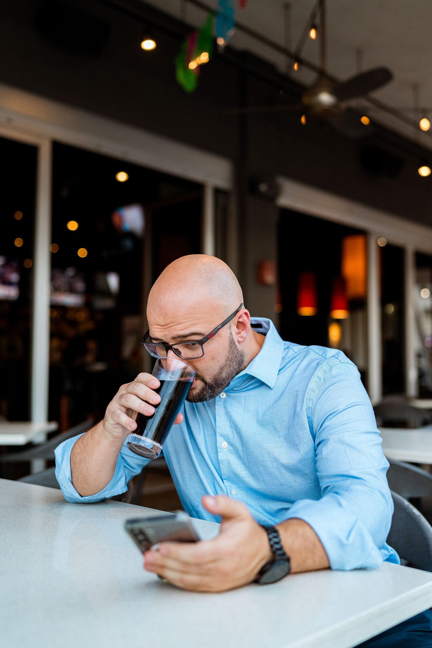 Person in light blue dress shirt looking at mobile phone while sitting at desk with ambient lighting.