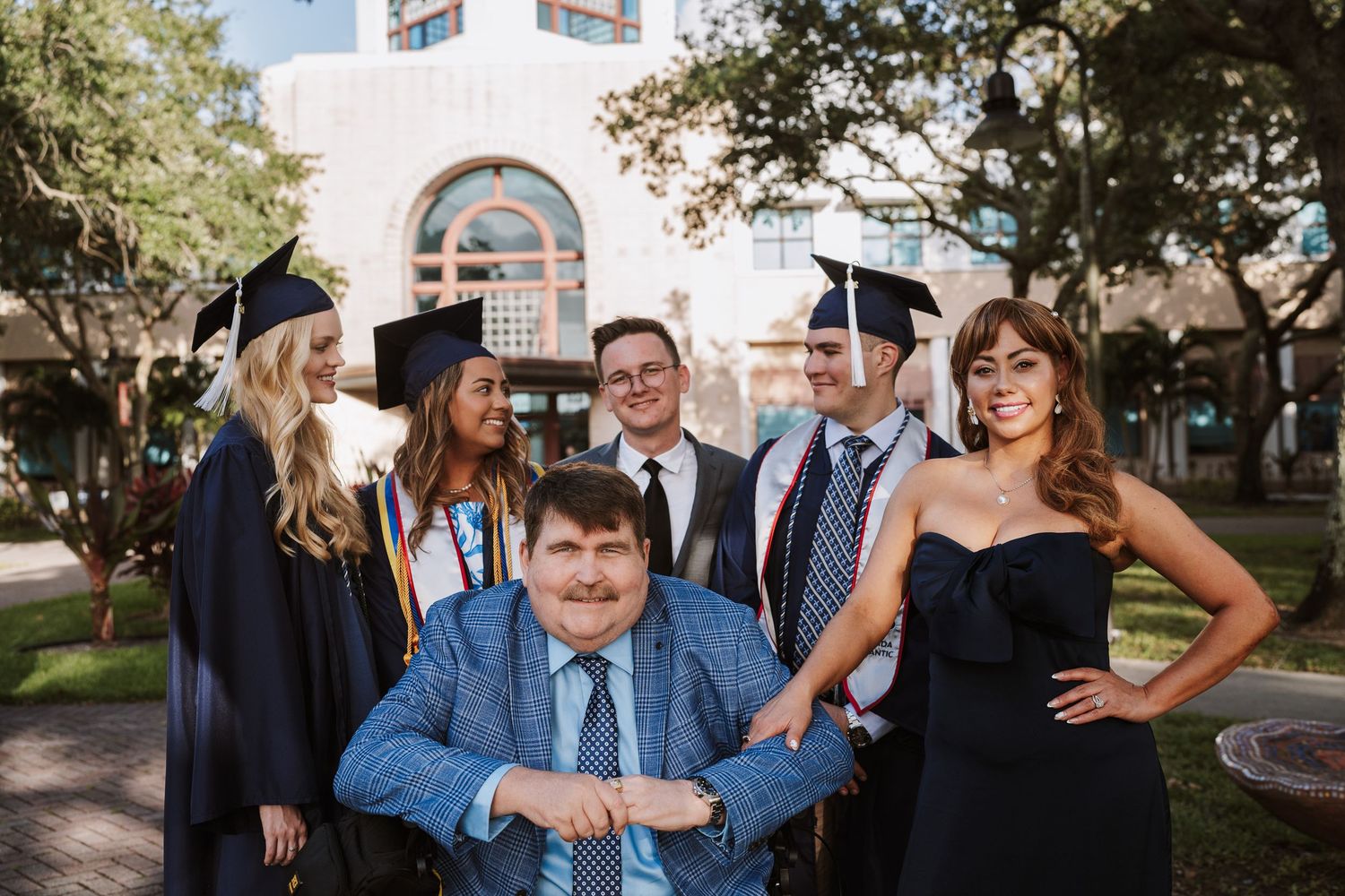 Group of graduates in caps and gowns celebrating outdoors on campus. graduation photos