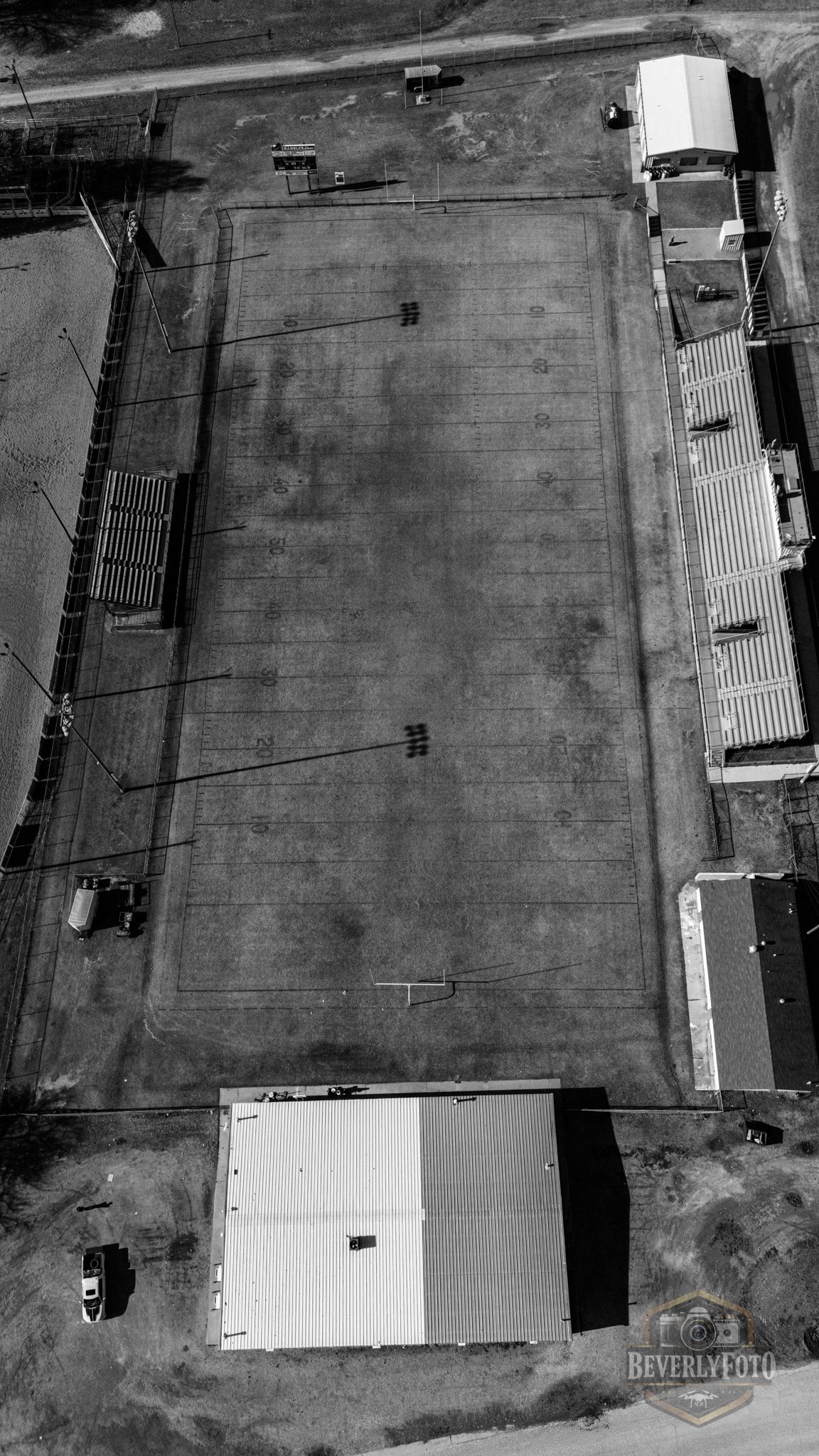 Aerial black and white view of a concrete sports court or field surrounded by buildings and structures.