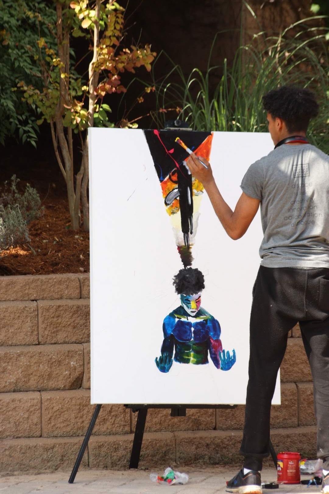 Artist working on white canvas against brick wall in outdoor setting.