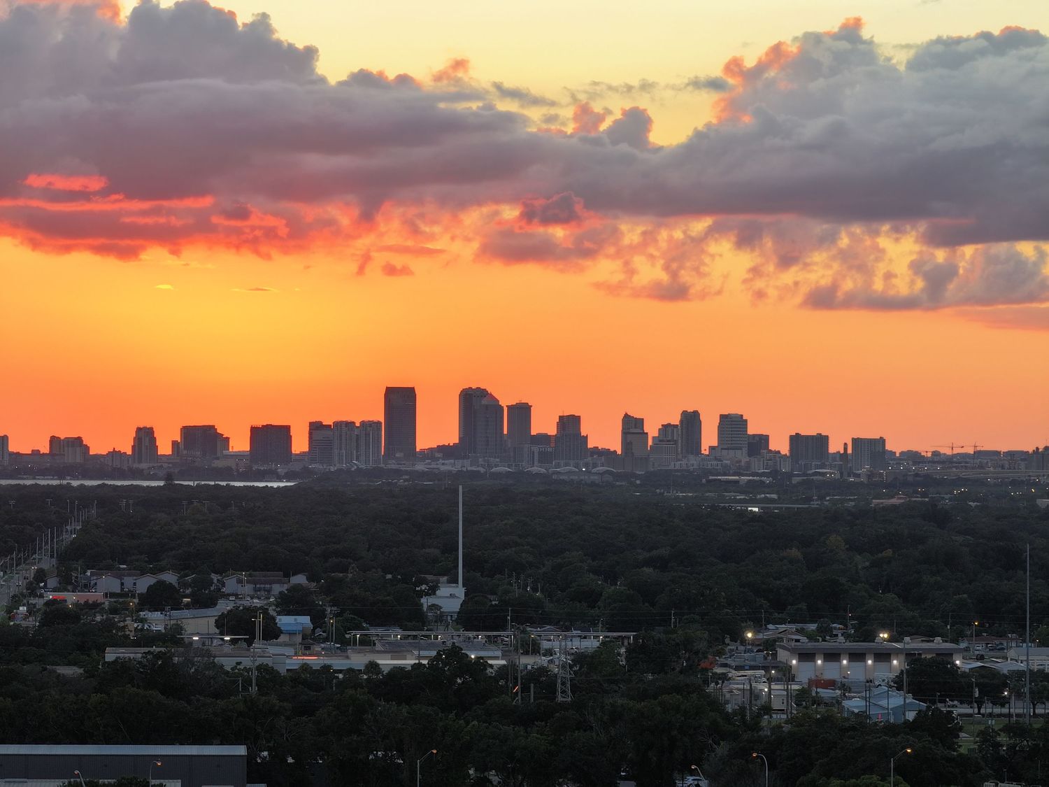City skyline silhouetted against a dramatic orange and purple sunset with clouds.