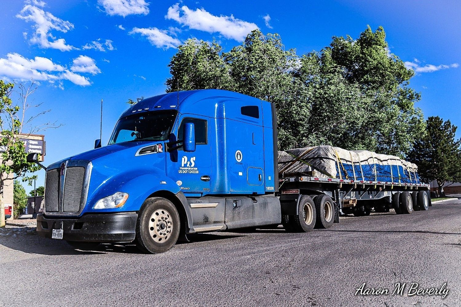 Blue Kenworth semi truck with tanker trailers on sunny day.