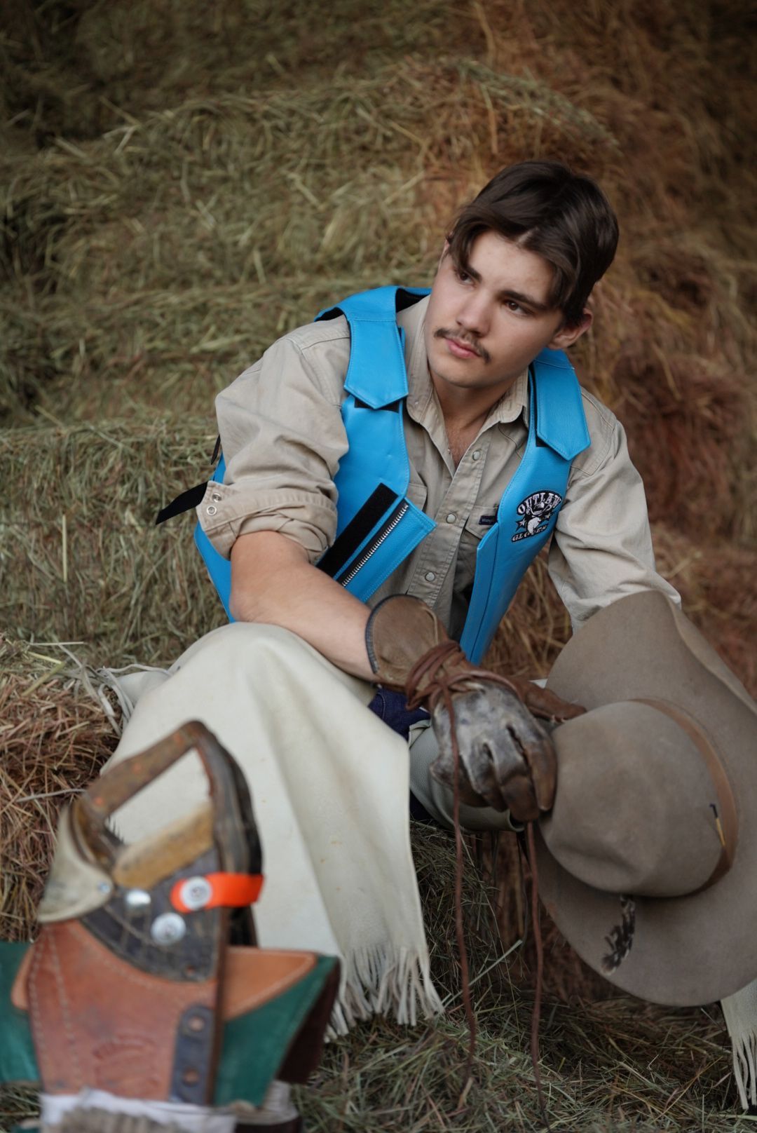 Person wearing gloves and a blue backpack examines something on the ground in an outdoor setting.