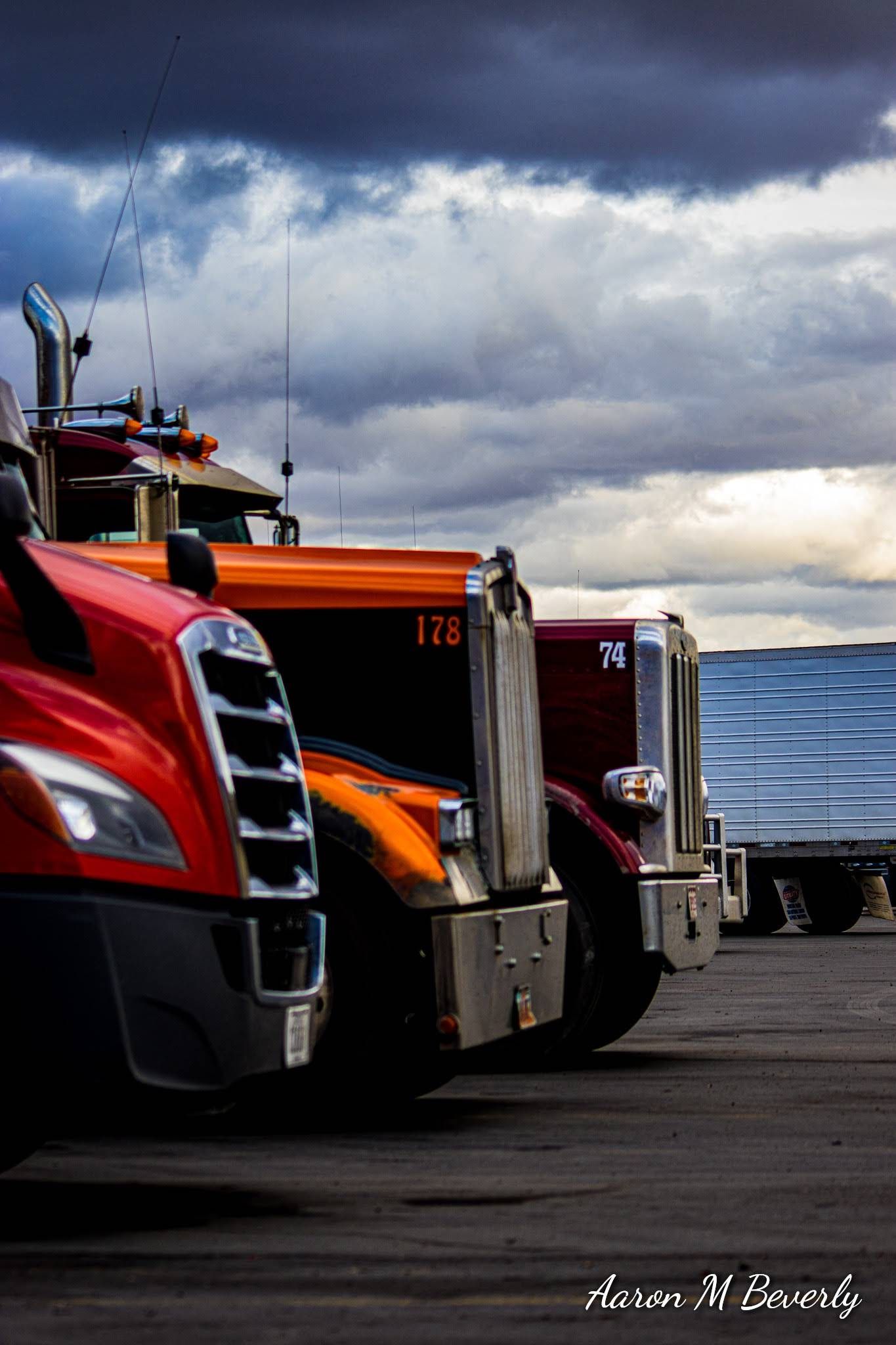 Line of semi truck cabs parked under dramatic stormy skies.