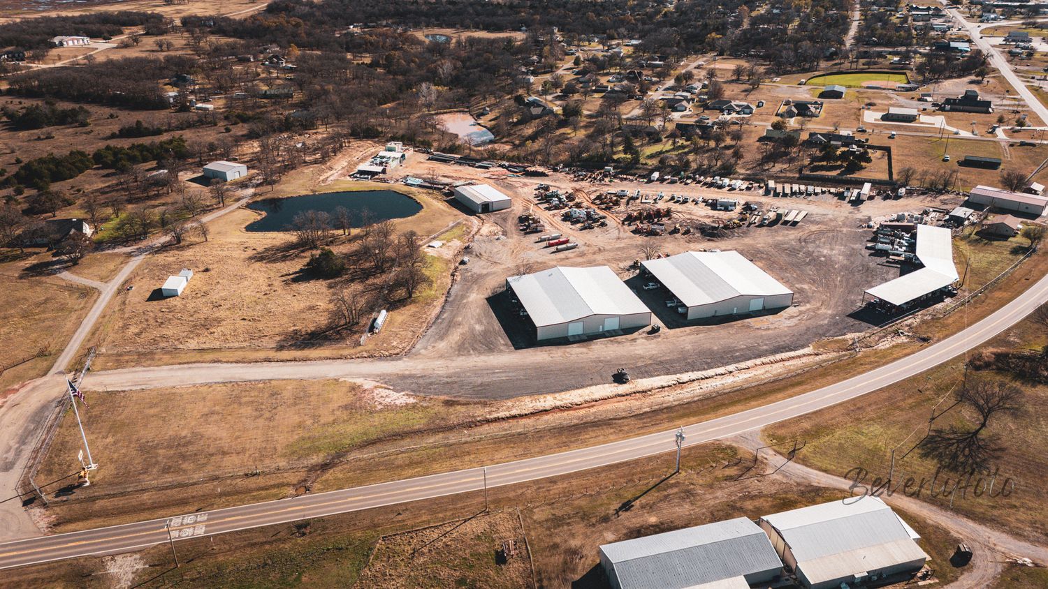 Aerial view of industrial warehouses and storage facilities along a curved road with surrounding rural landscape.