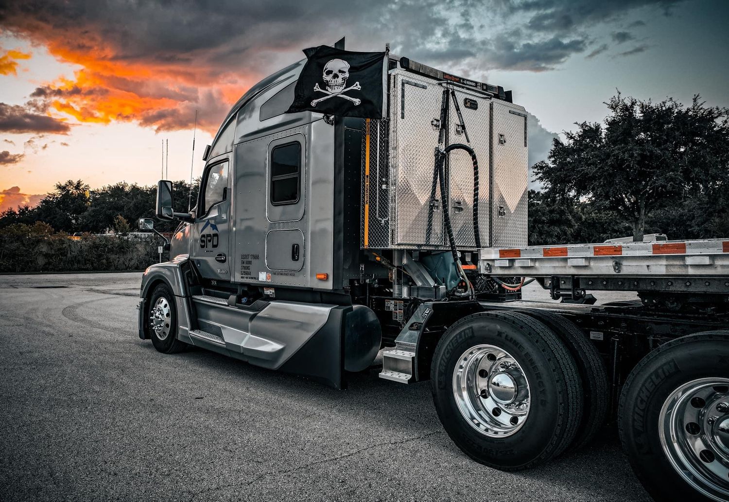 Semi truck cab with skull and crossbones design against dramatic sunset sky.