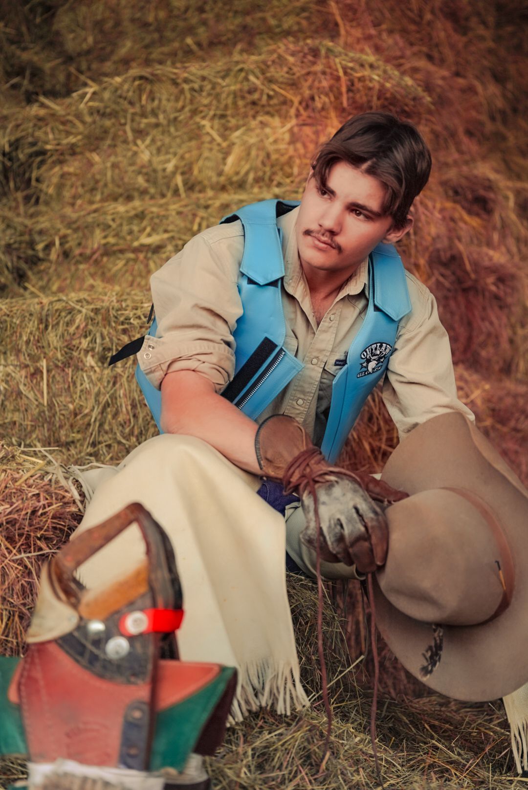 Person in beige coat and blue vest crouches while handling equipment outdoors.