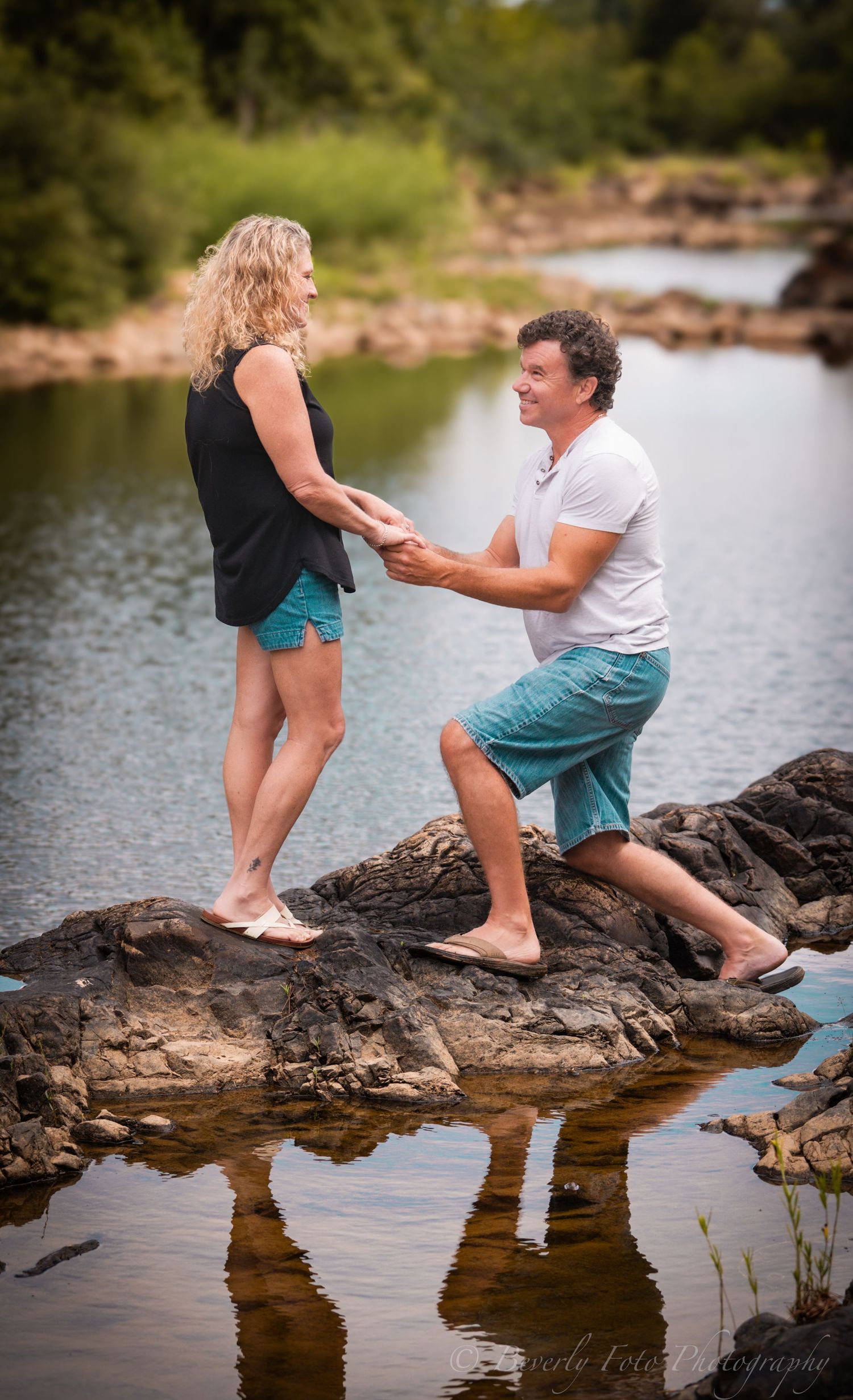 A romantic proposal moment captured on rocky outcrop by a serene lake during summer.