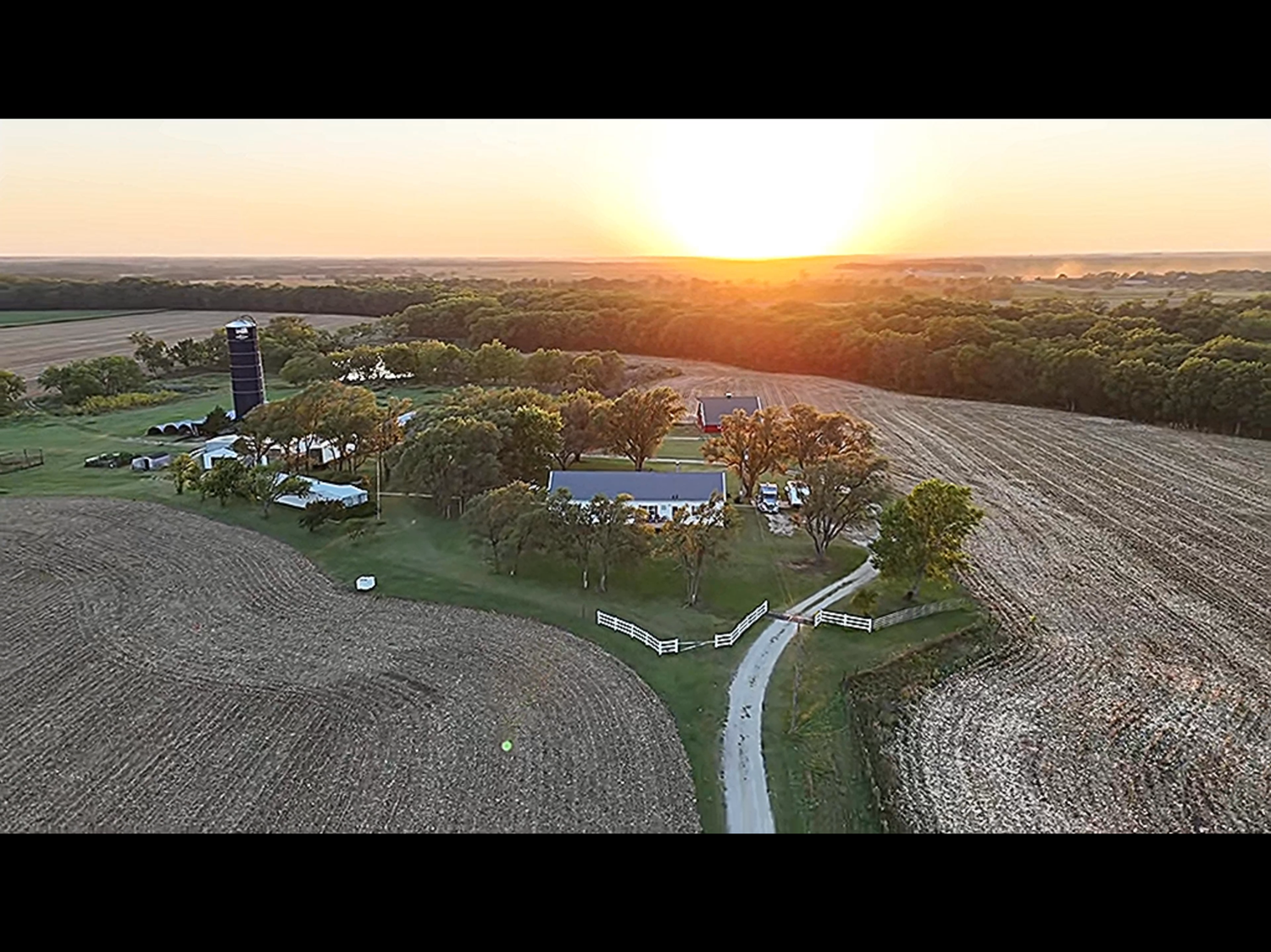Aerial view of a rural farm property with winding road and fields during golden sunset.