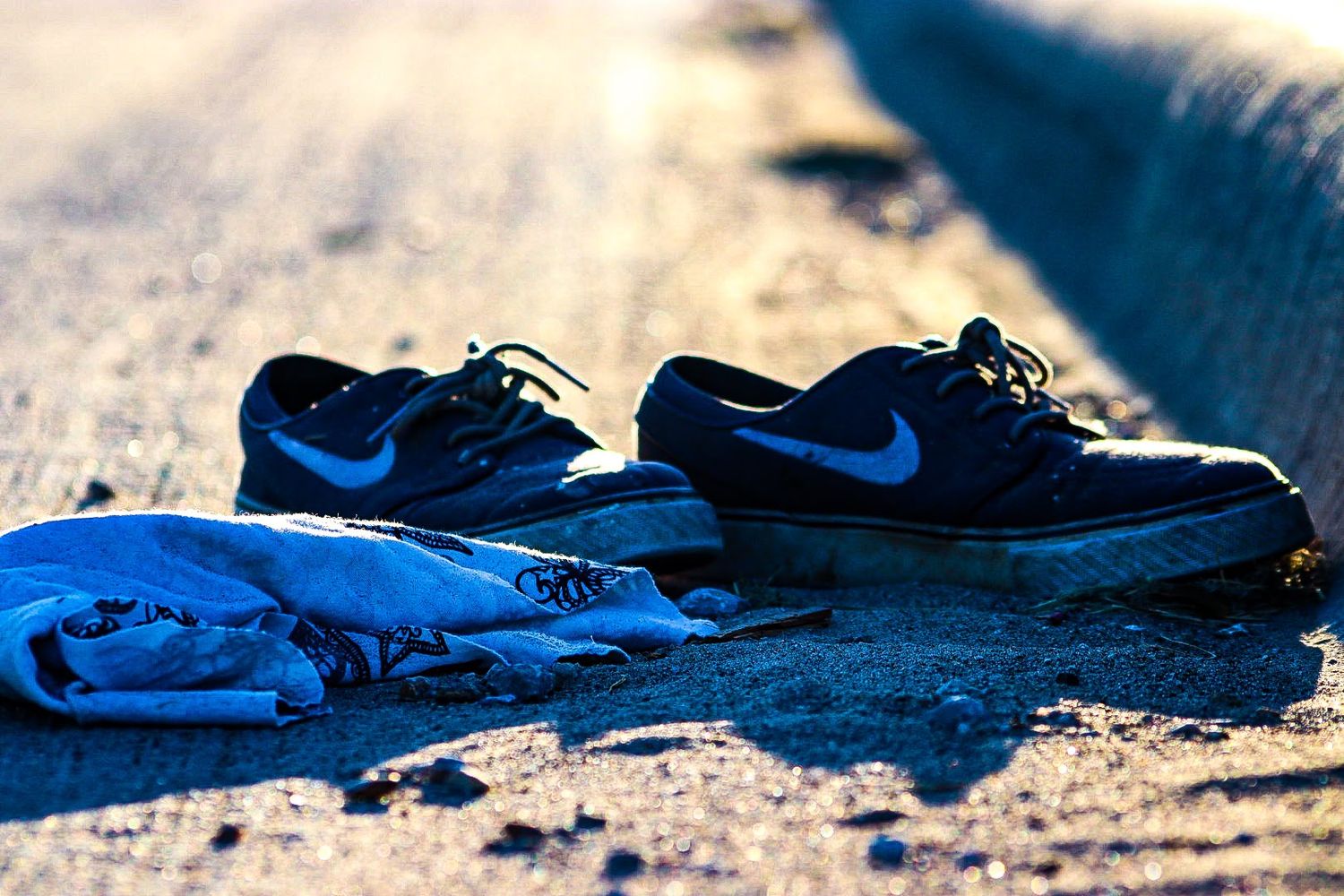 Abandoned black shoes and blue clothing items scattered on a rough concrete surface in dramatic lighting.