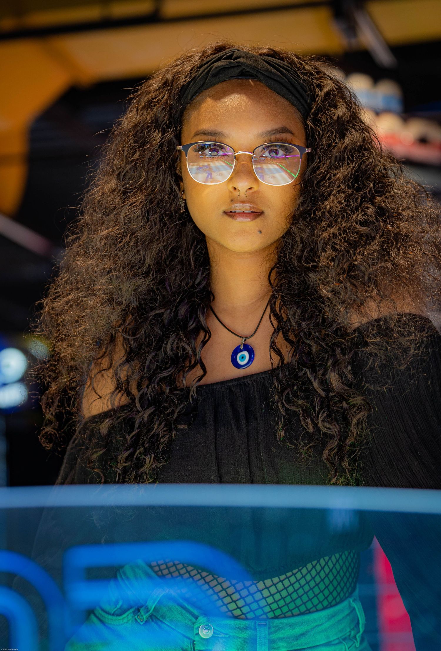 Woman with curly dark hair and glasses wearing a black top against a dark background.