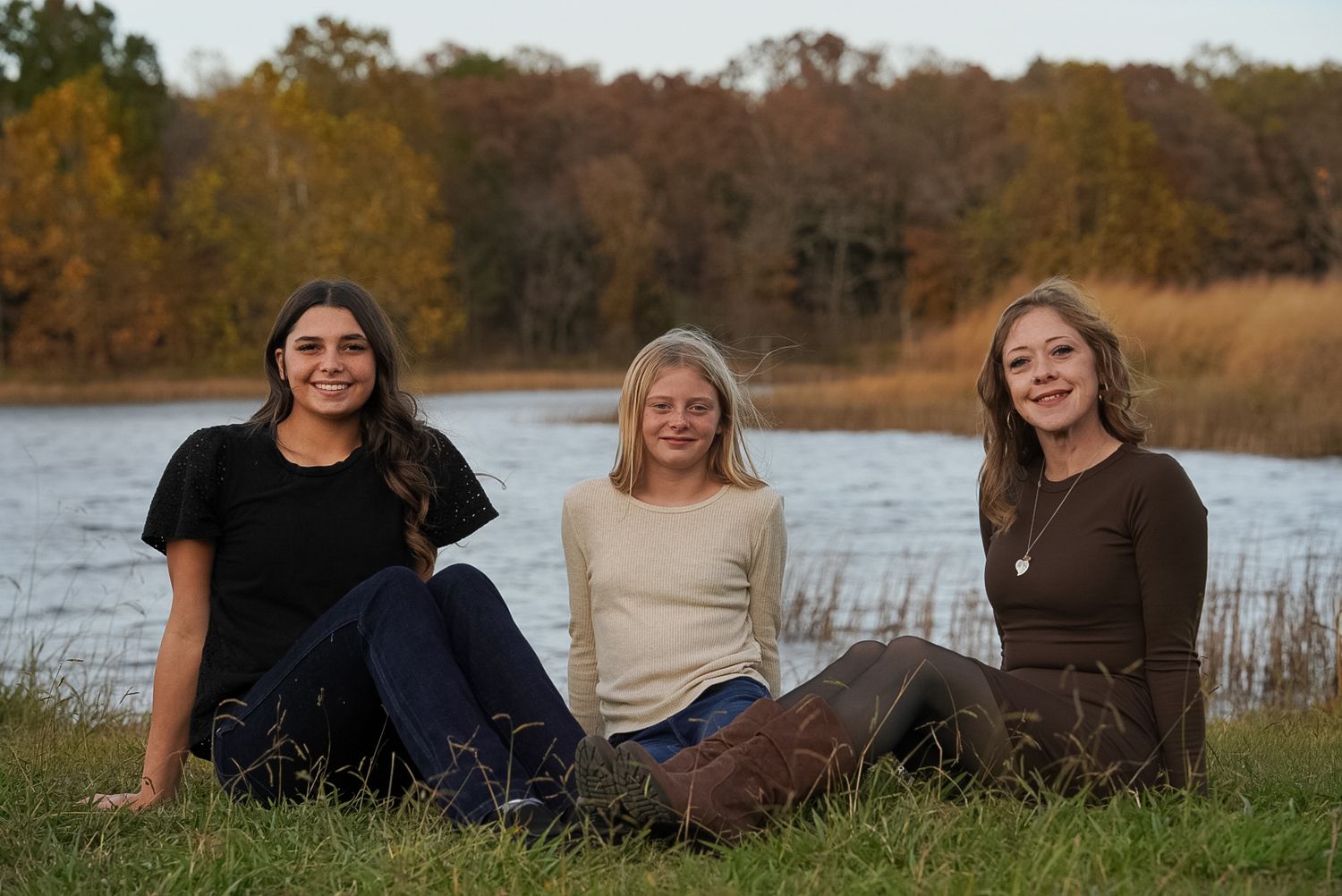 Group relaxing together on grass near a lake during sunset.