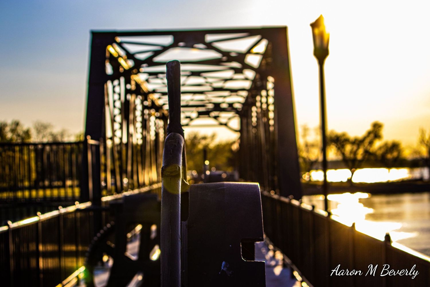 Bridge silhouetted against golden sunset with metal structure creating dramatic shadows.