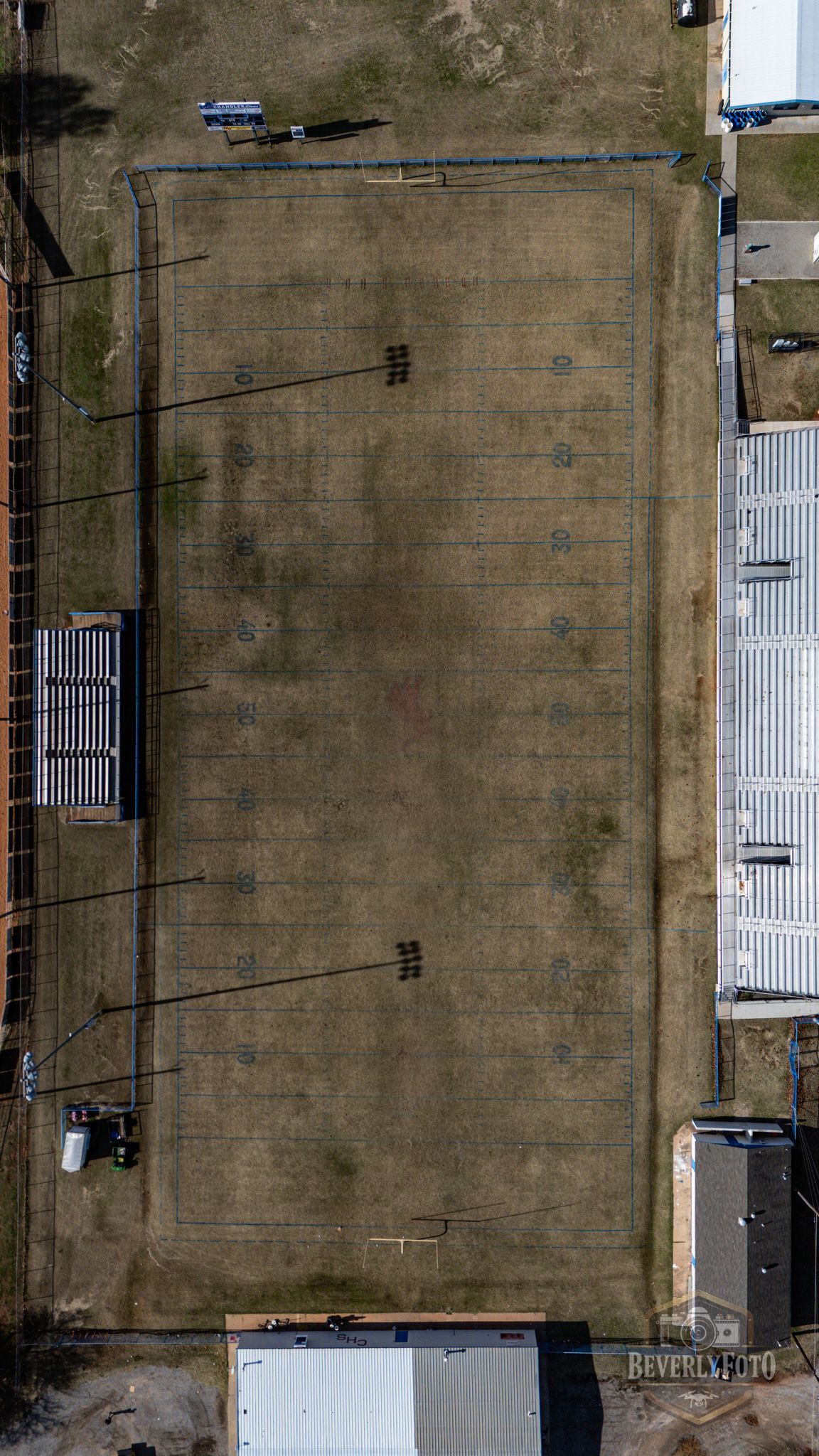 Aerial view of a brown dirt field with white structures and power lines visible from above.
