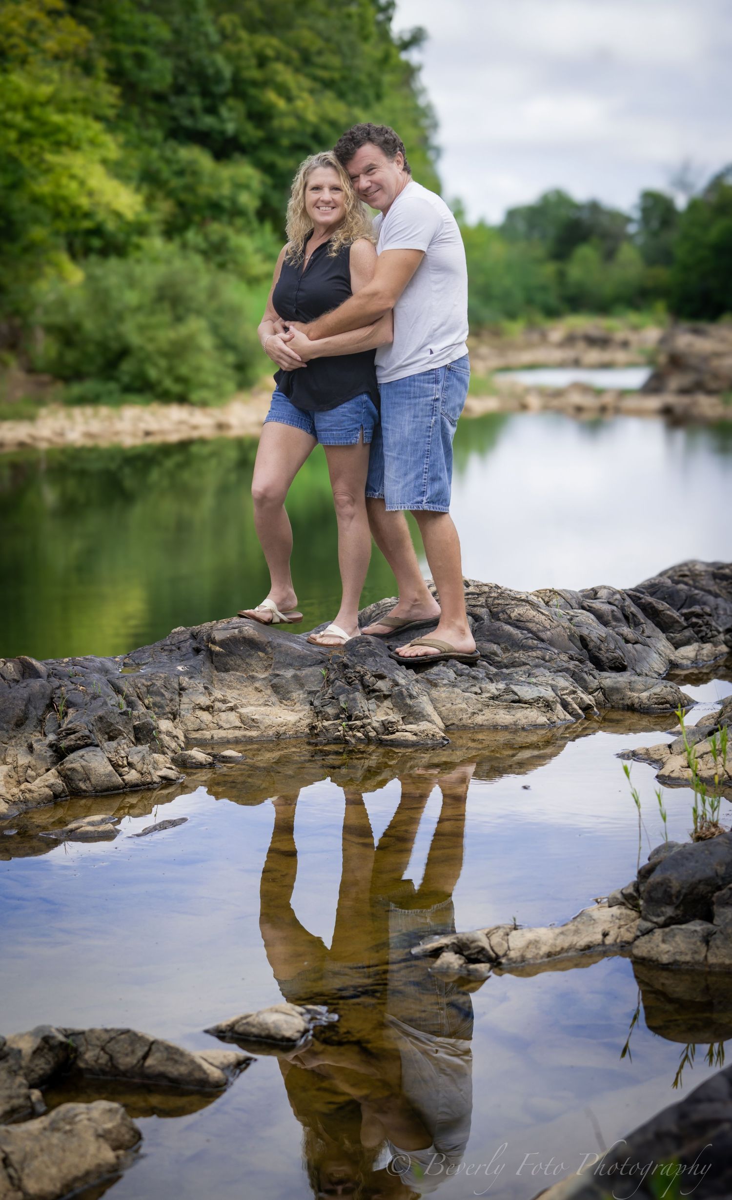 Couple sitting on rocky outcrop over reflective water.