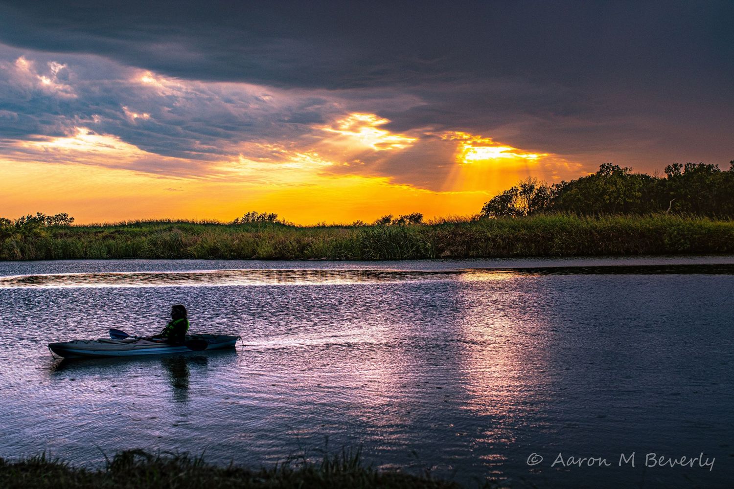 Silhouette of kayaker on calm lake during dramatic orange sunset.