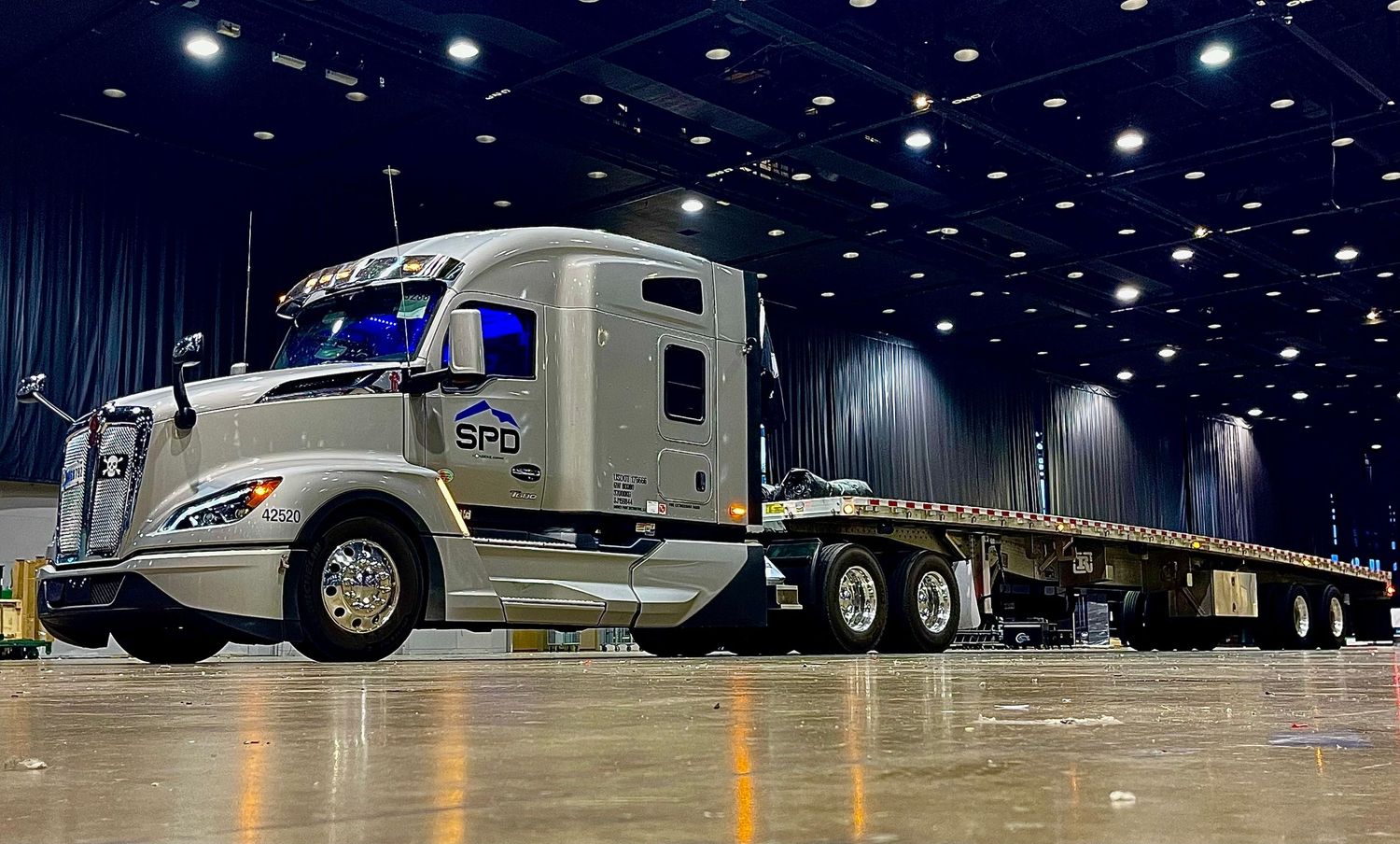 Modern silver semi truck displayed in illuminated indoor showroom.