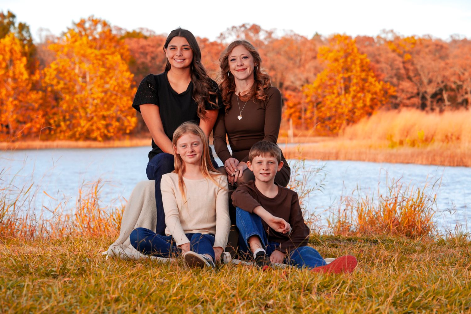 Family portrait session in autumn with vibrant orange foliage and lakeside setting at sunset.