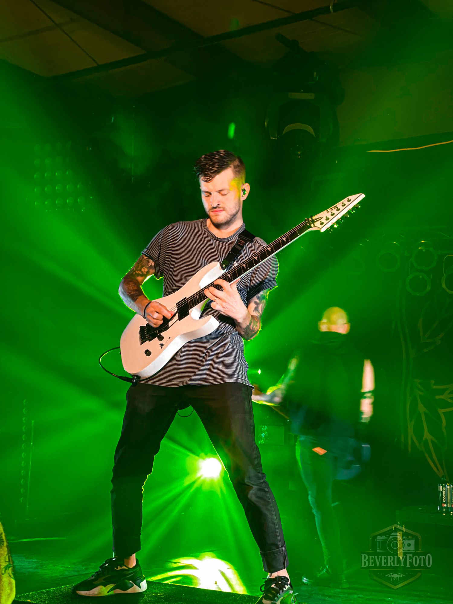 Concert stage bathed in green lighting shows musicians performing with electric guitars.
