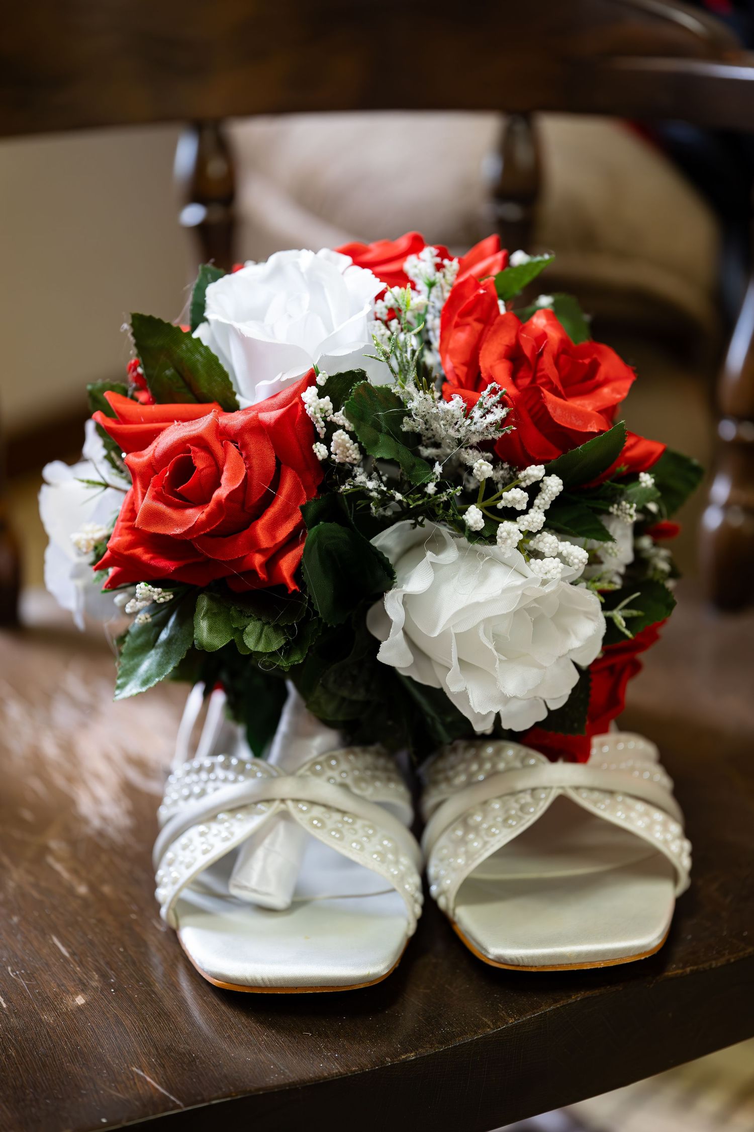 White and red roses arranged in elegant bridal shoes on a wooden surface.