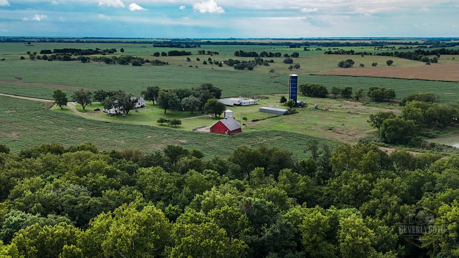 Aerial view of a rural farm with red barn and silo surrounded by green fields and forest on a sunny summer day.