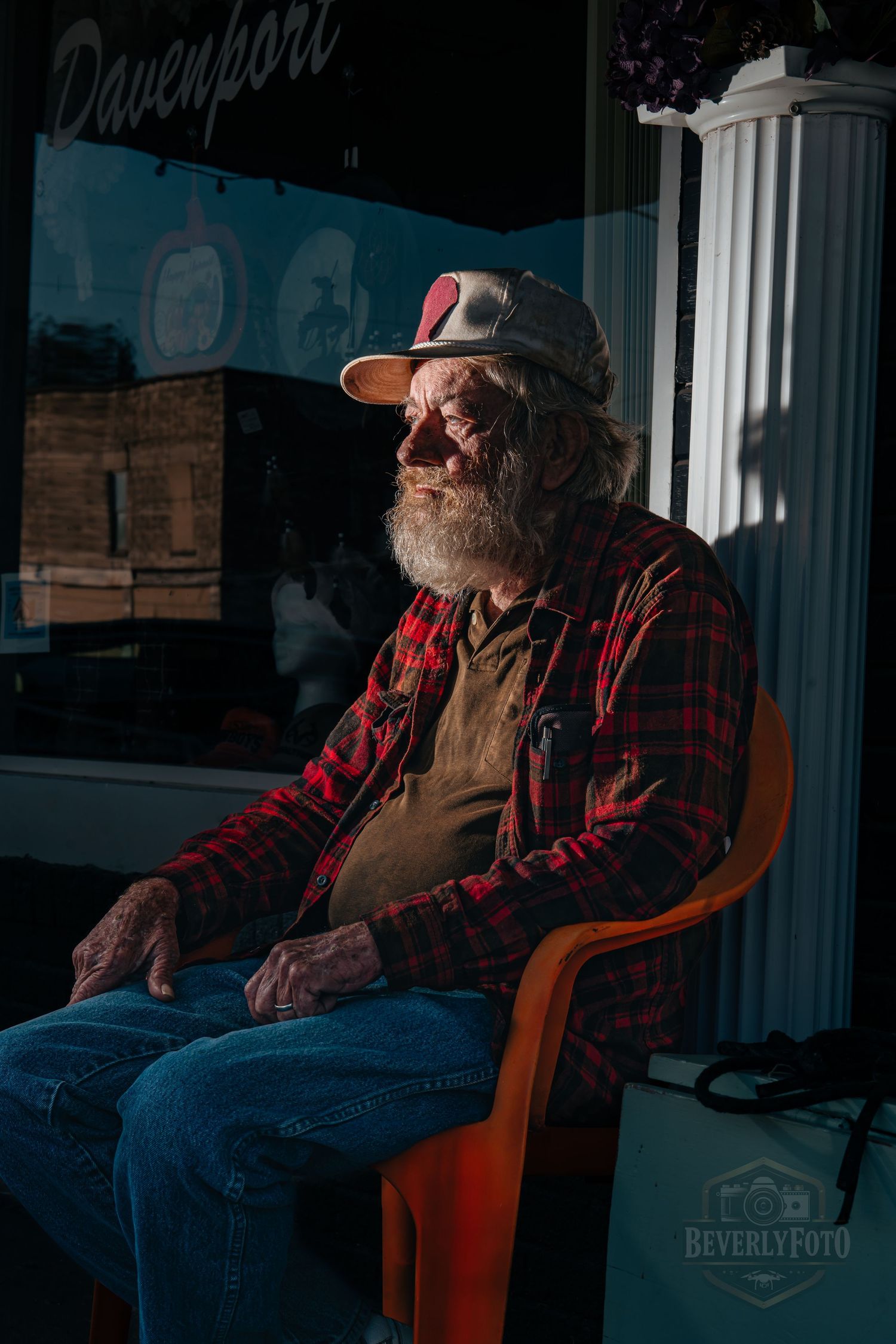 Person in red plaid shirt and sunglasses relaxes in orange chair while sunlight streams through window.
