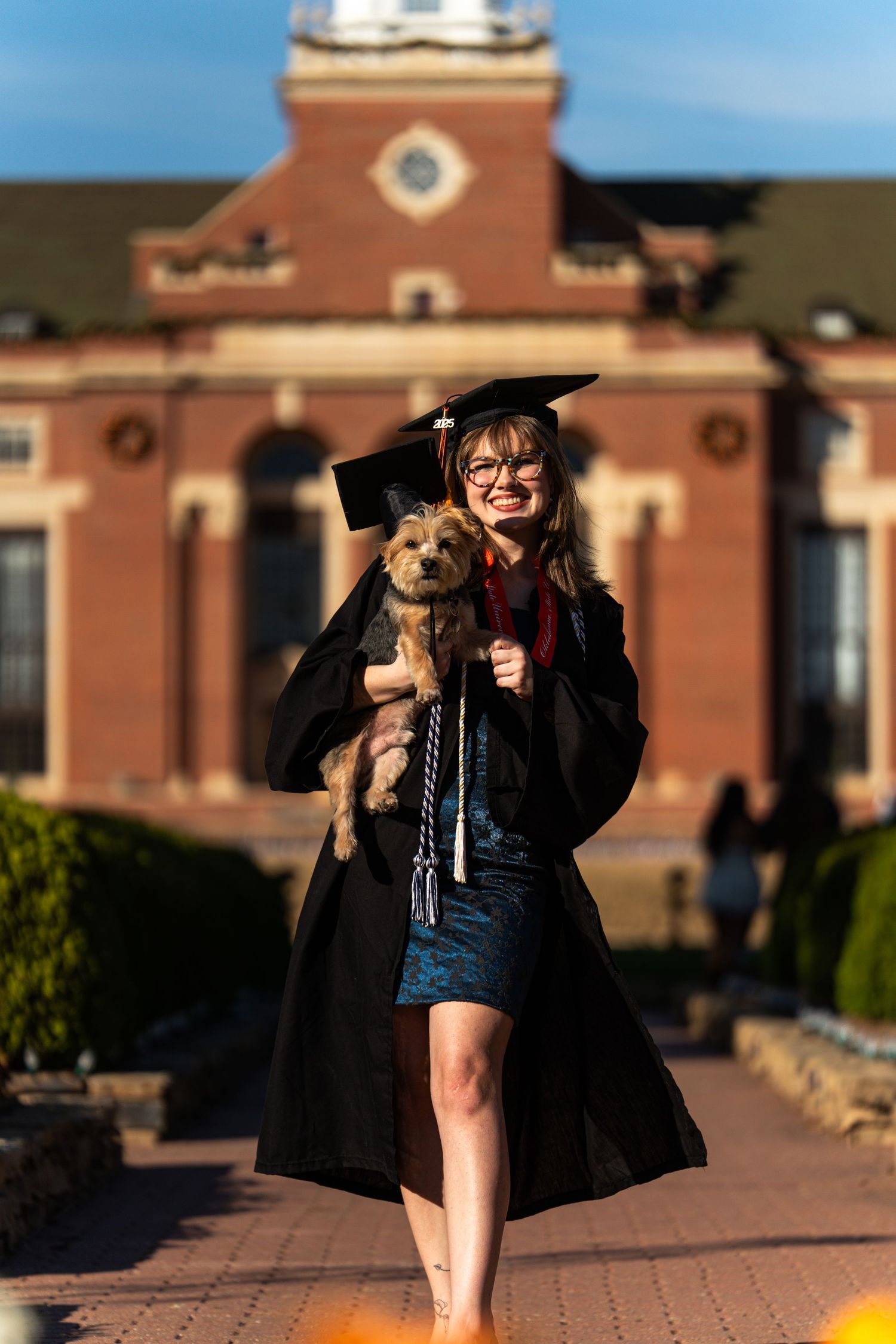 Graduation photoshoot featuring black cap and gown against brick building backdrop.