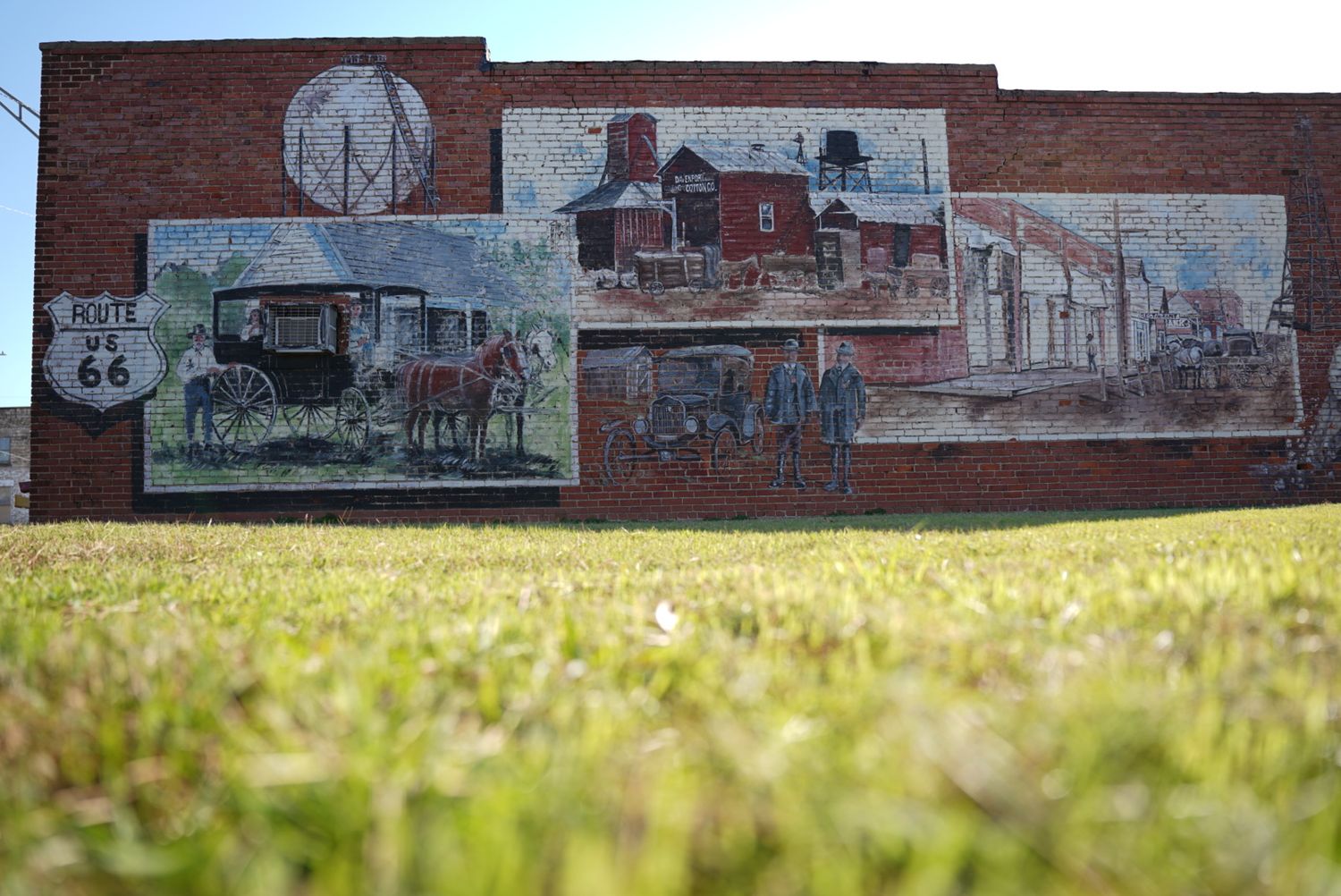 Historic mural depicting vintage transportation scenes painted on brick wall.