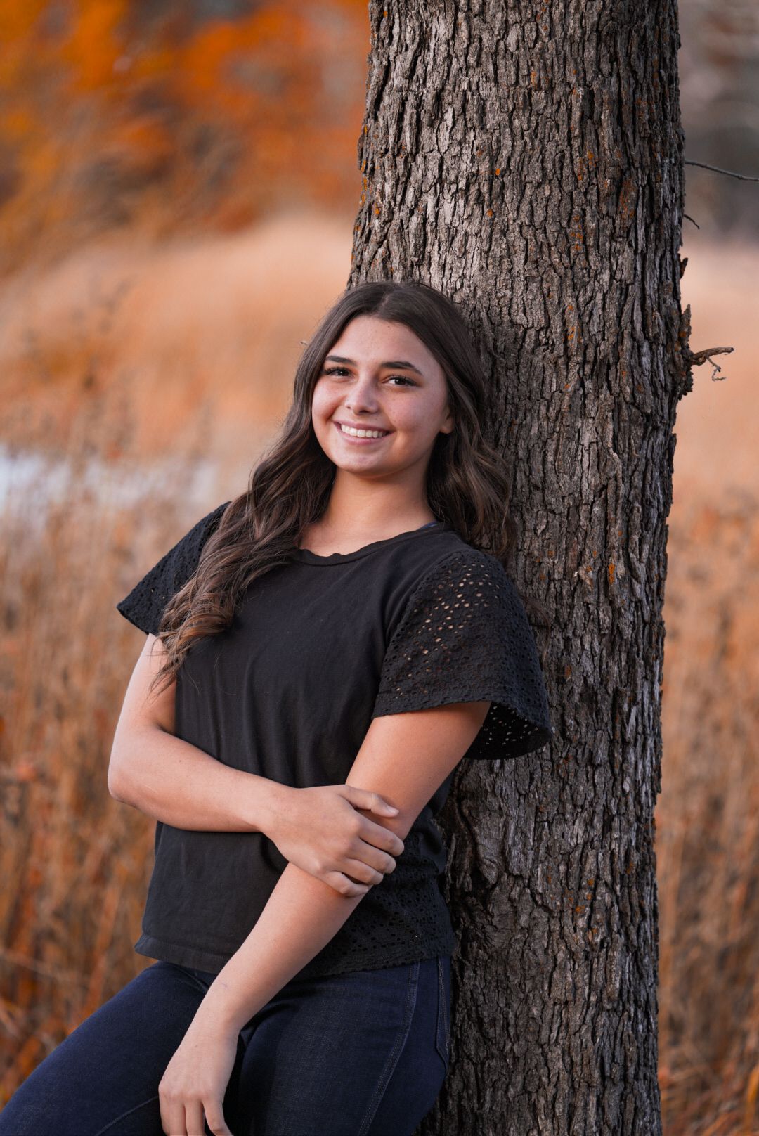 Portrait session against tree trunk with autumn orange background colors.