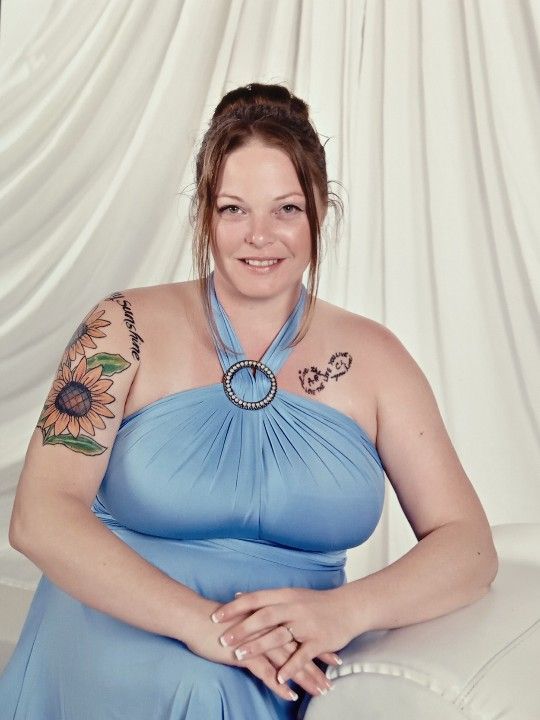 Portrait in a blue halter dress against white backdrop showing floral tattoo artwork.