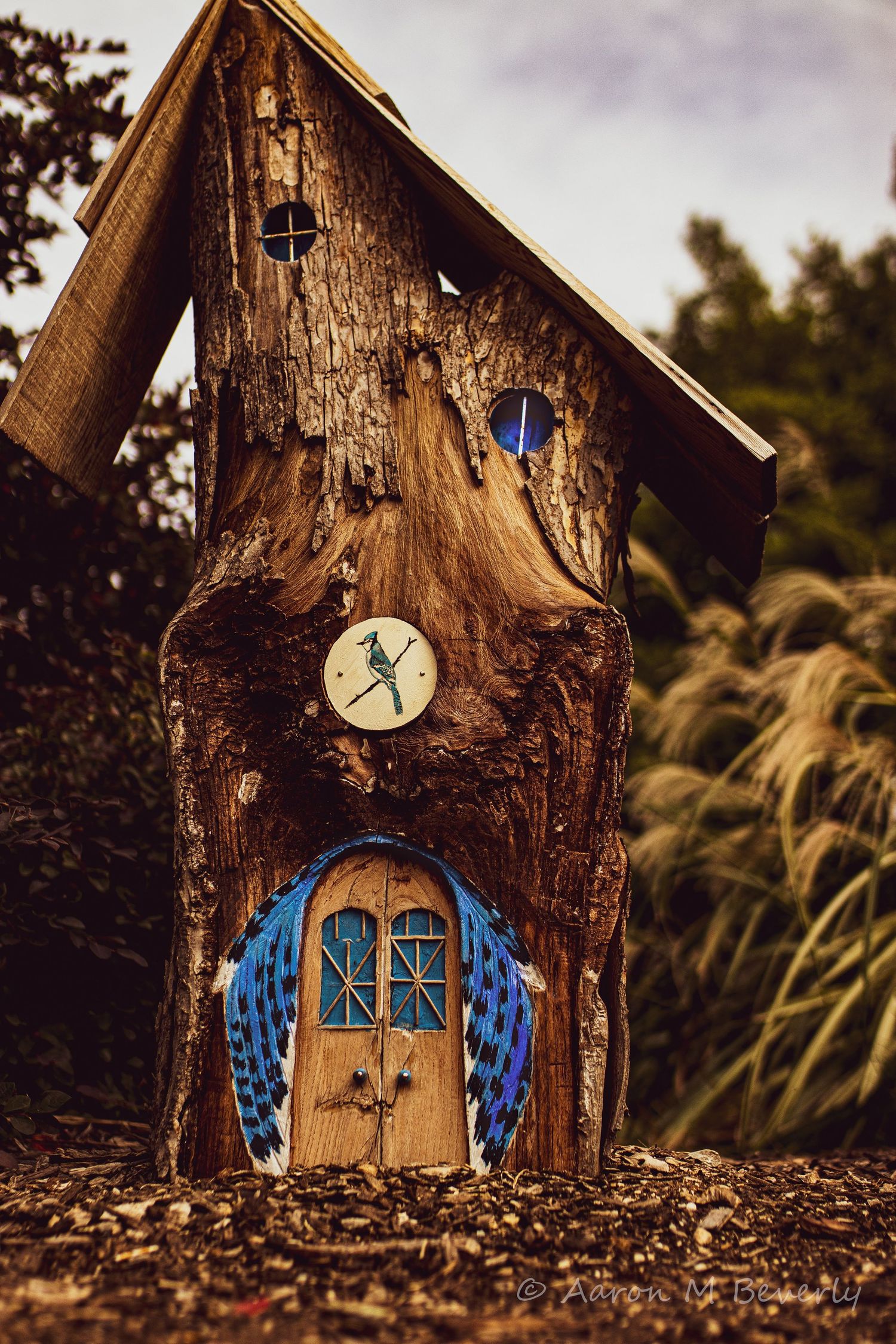 Miniature fairy house made from wood with blue doors and windows surrounded by autumn leaves.