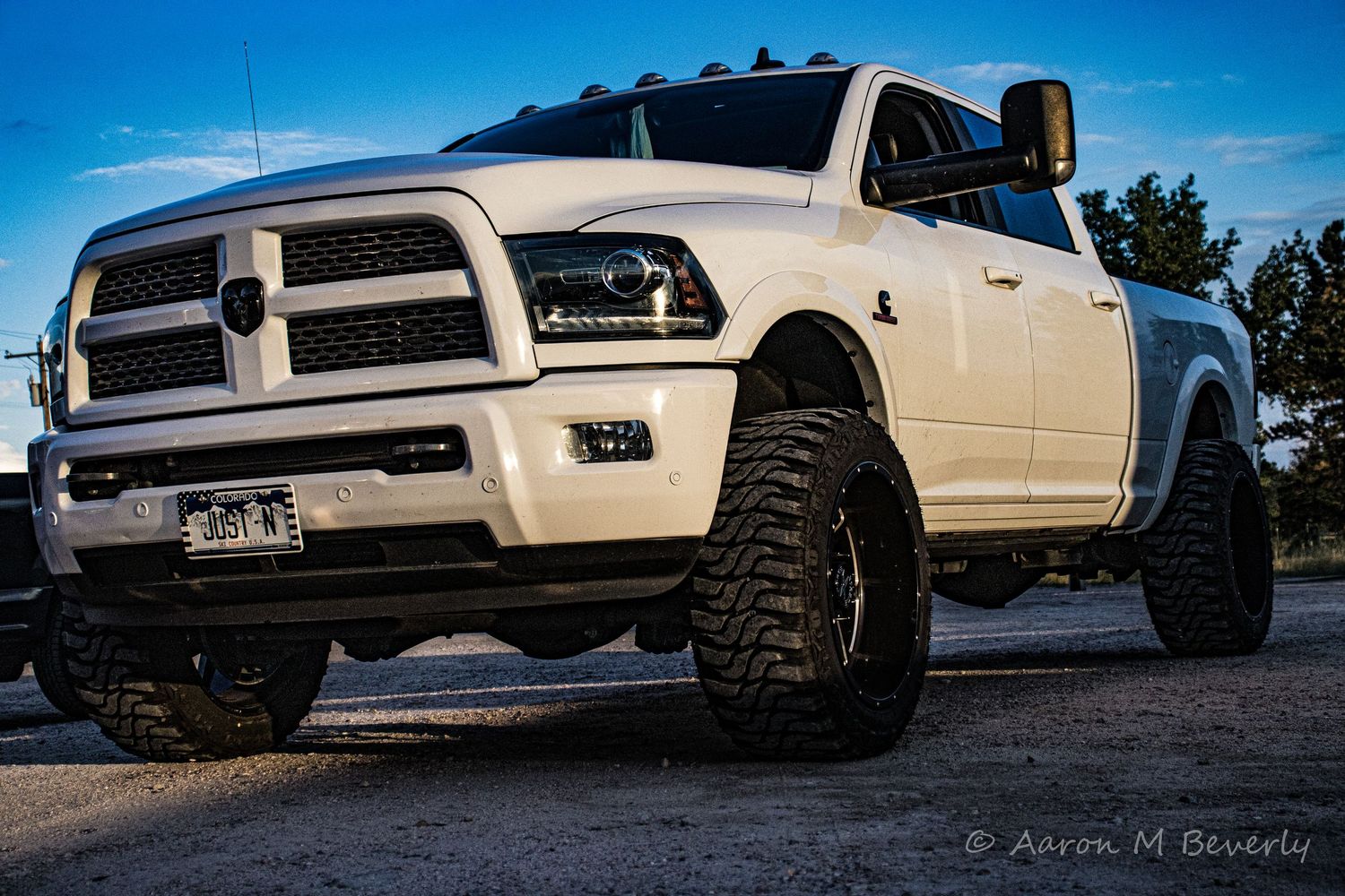 White lifted pickup trucks with off-road tires lined up against a blue sky backdrop during sunset.