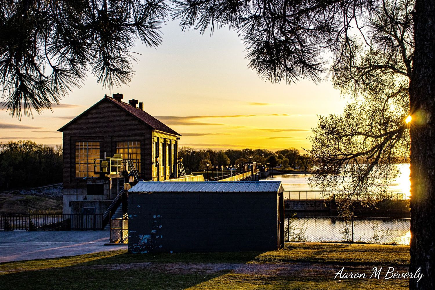 Historic building silhouetted against golden sunset with pine trees framing the scene.