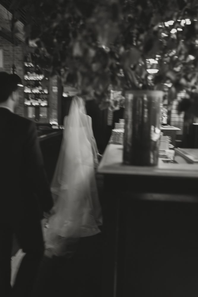 black and white image of bride walking with veil inside restaurant