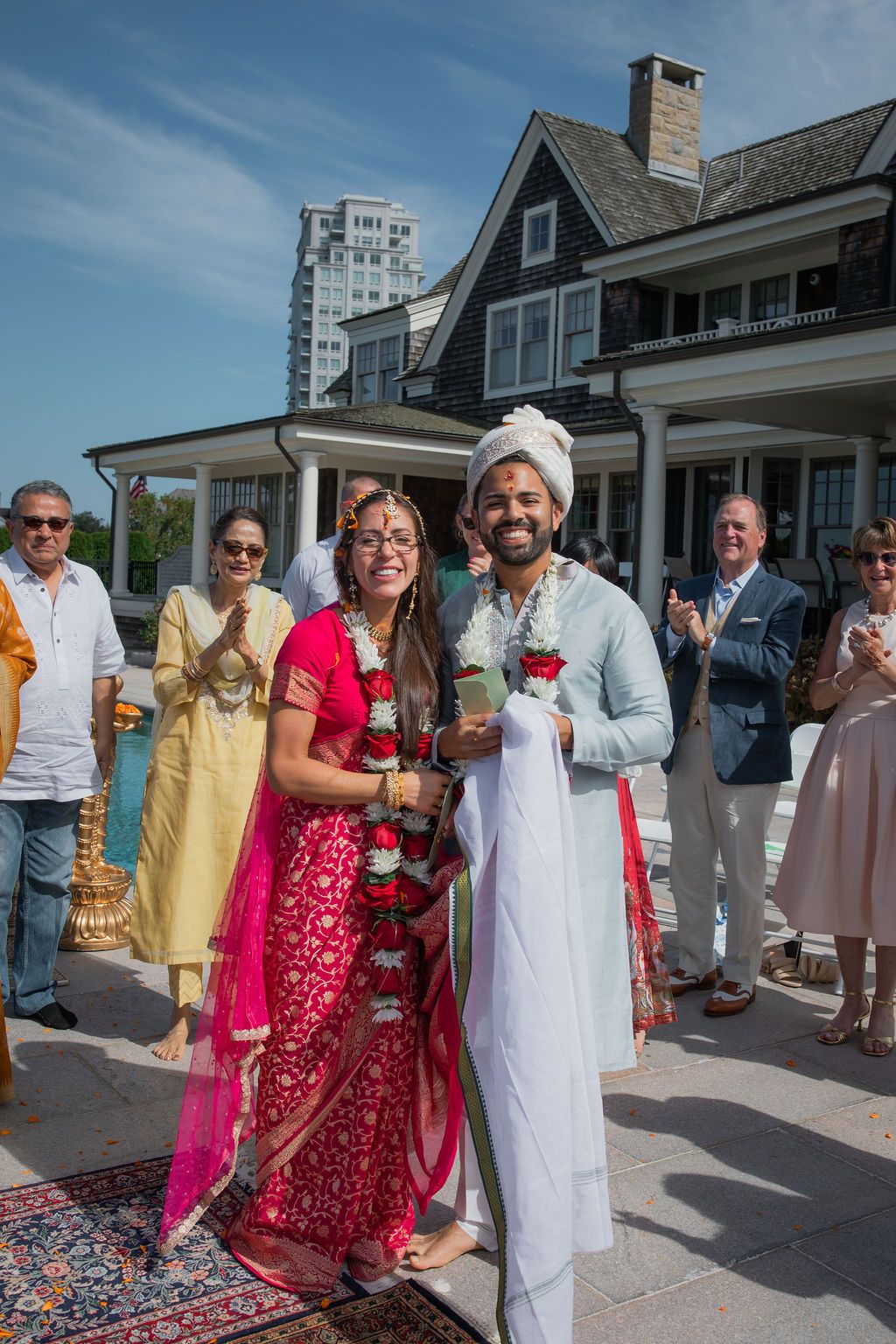 indian bride and groom smile at  camera with family behind them
